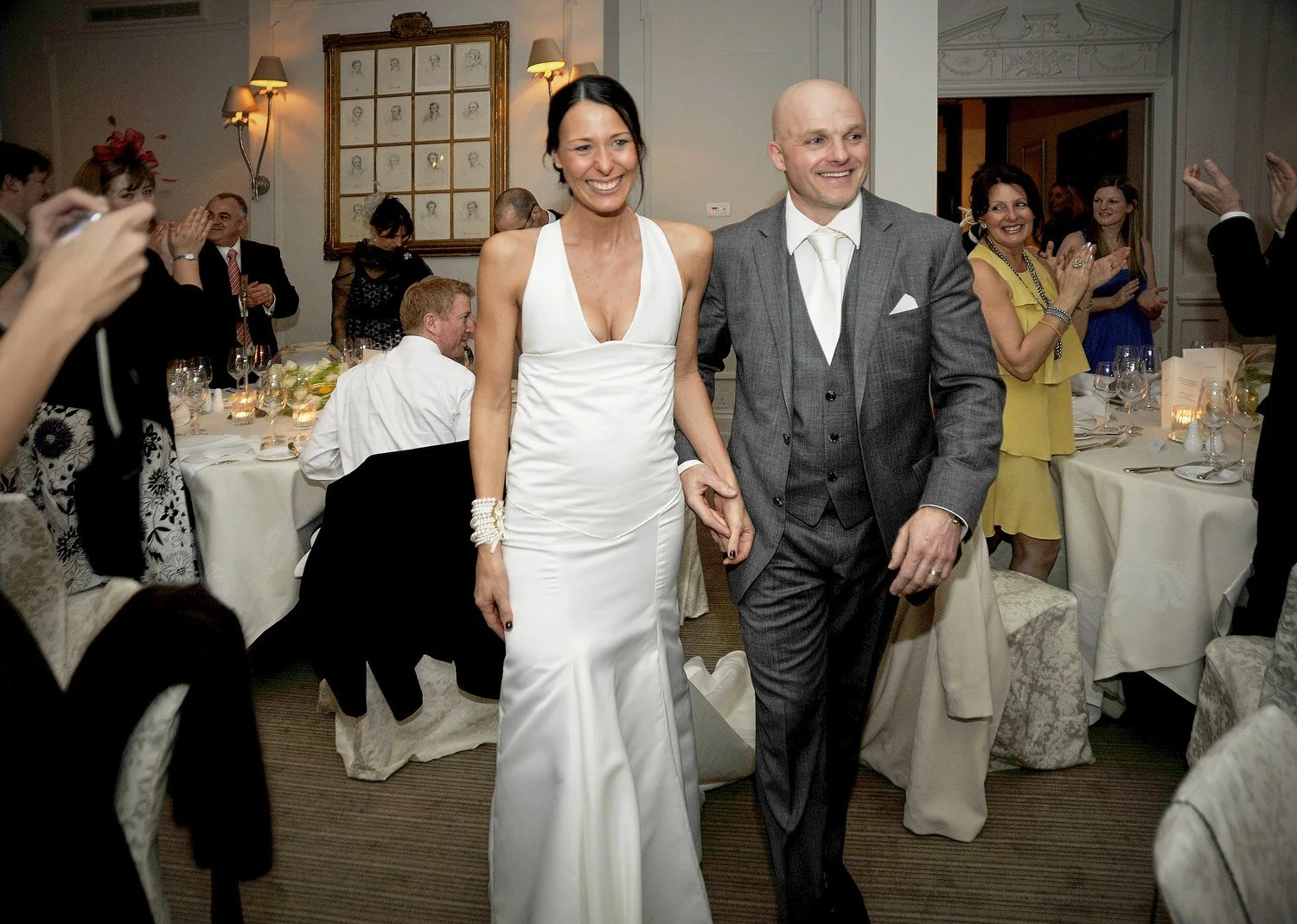 Bride and groom walk through dining room as guests clap their arrival.
