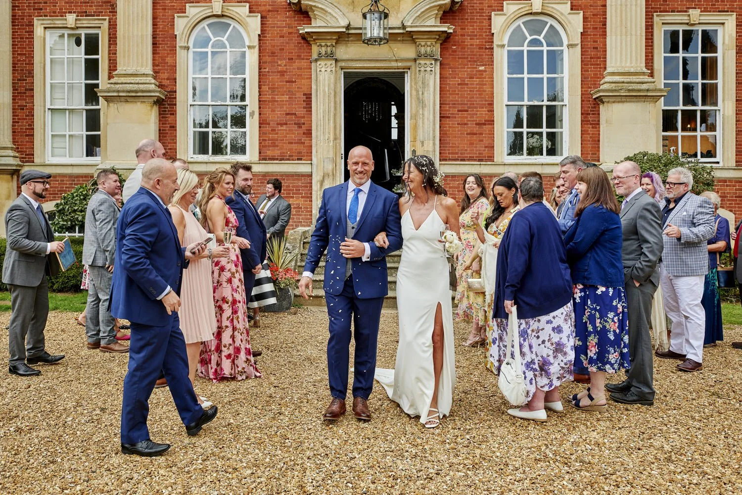 Bride and groom greet guests outside on a gravel driveway.