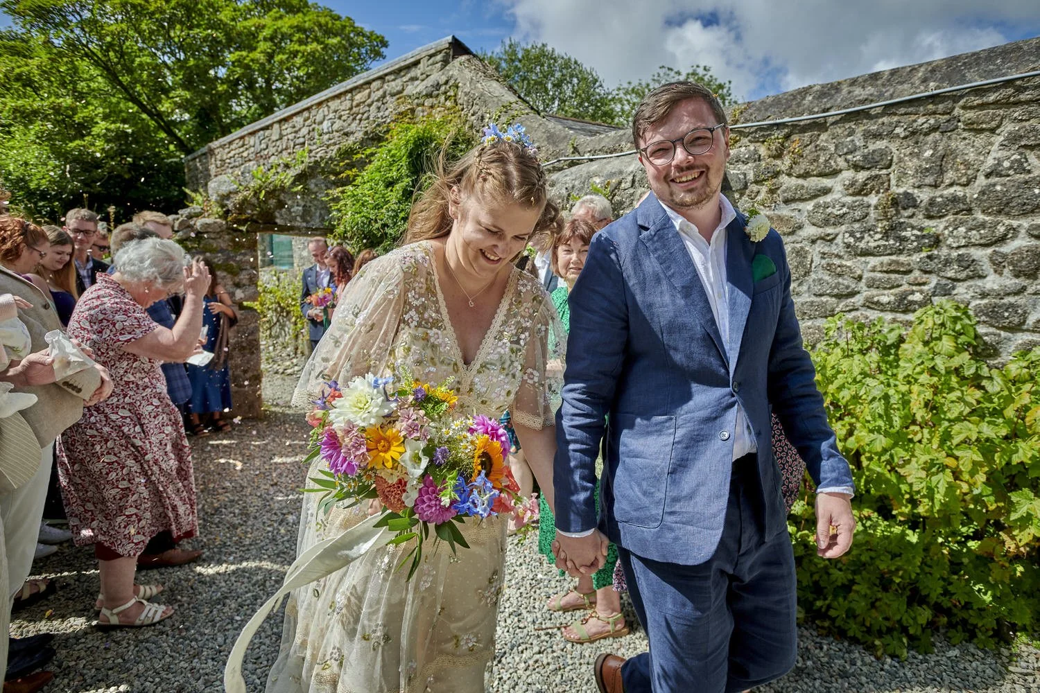 Close up view of bride and groom leaving crowd of friends and guests covered in confetti.