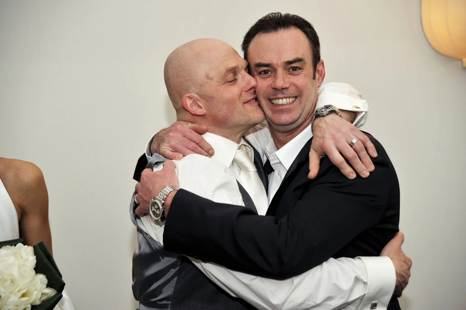 Groom and best man hug and smile at the camera.