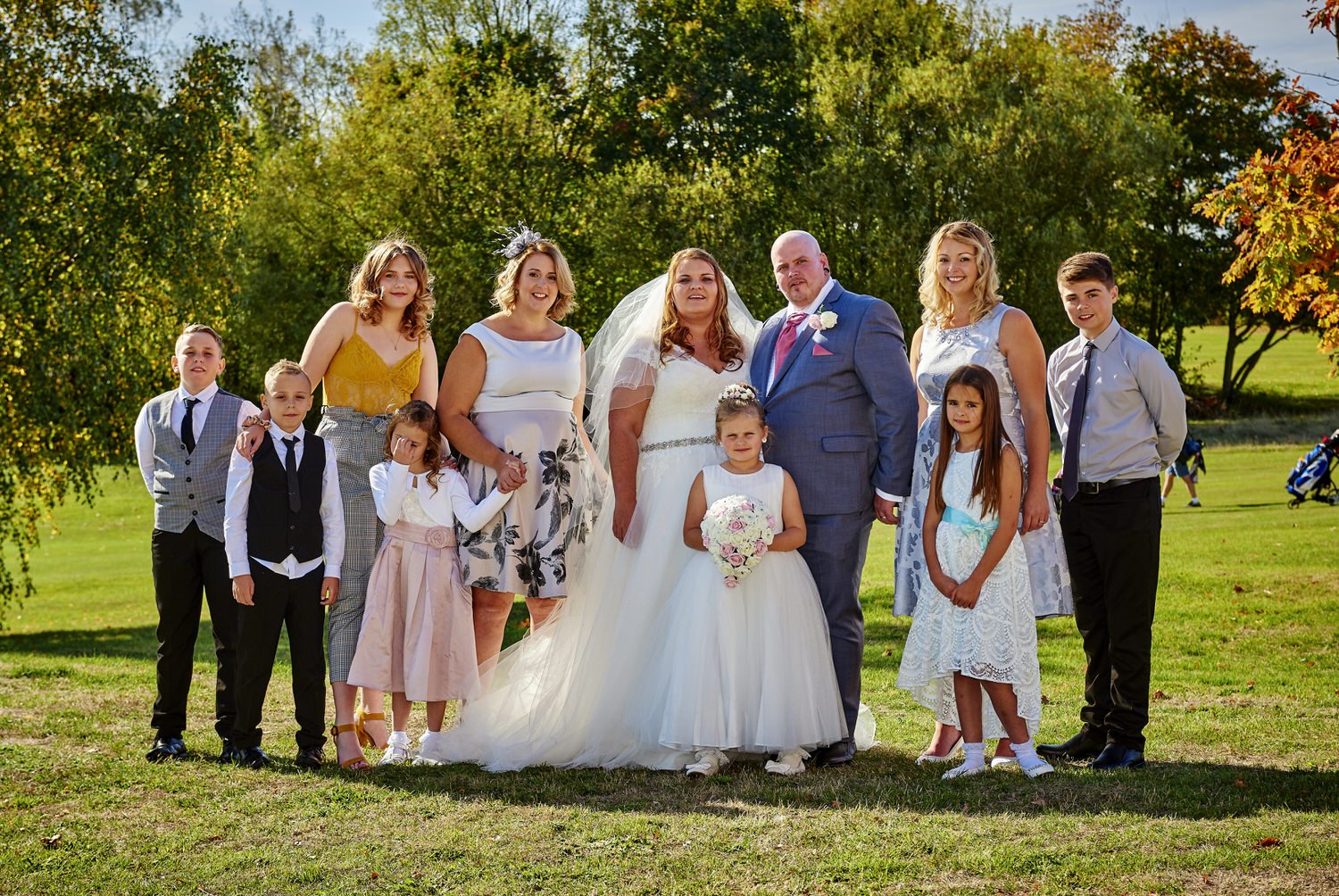 A formal group of friends stand for a photograph with trees behind them.