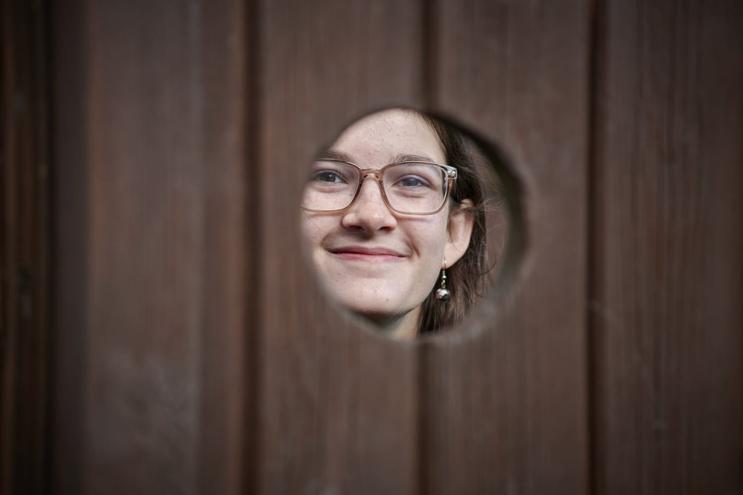 Guest peeks through a hole in a fence and smiles.