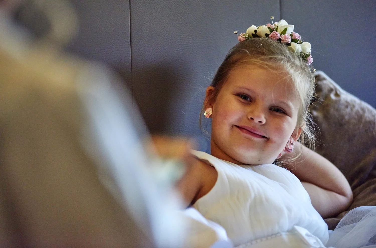 A young bridesmaid sits back in a comfy chair and smiles.