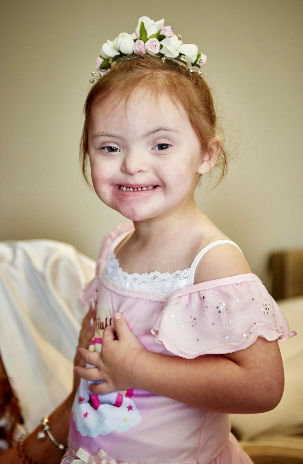 A young bridesmaid sits and smiles at the camera.