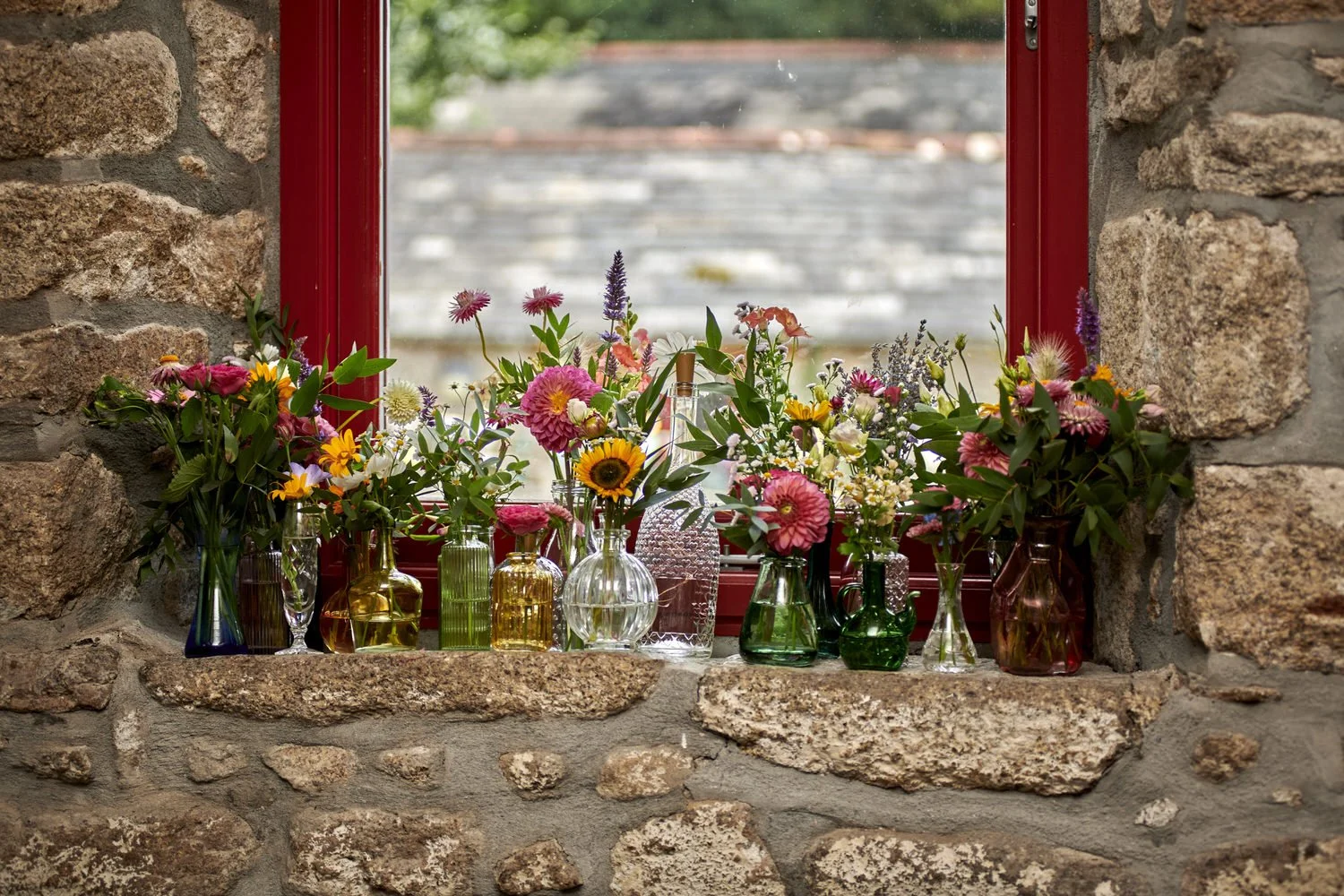A windowsill with lots of small vases of flowers.