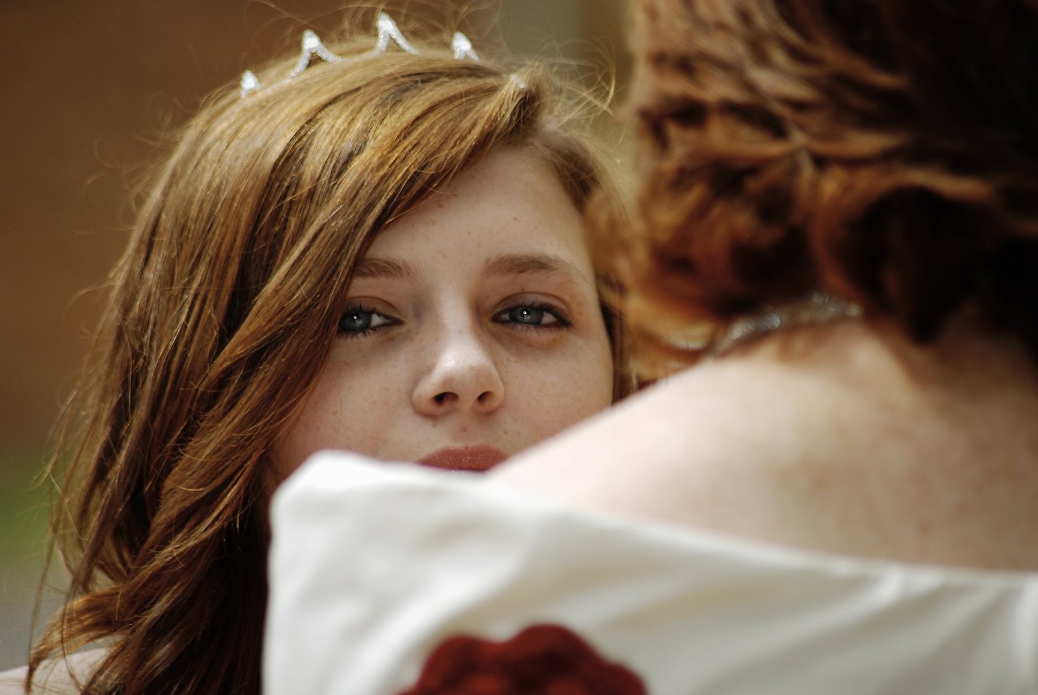 Bridesmaid smiles over bride’s shoulder during wedding prep.
