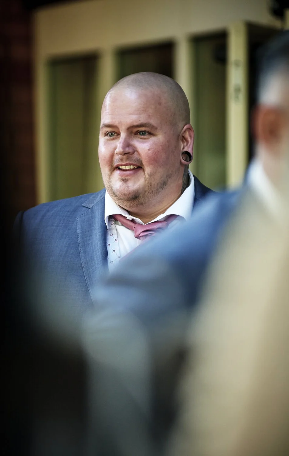 The groom smiles at his friends out of focus in the foreground.