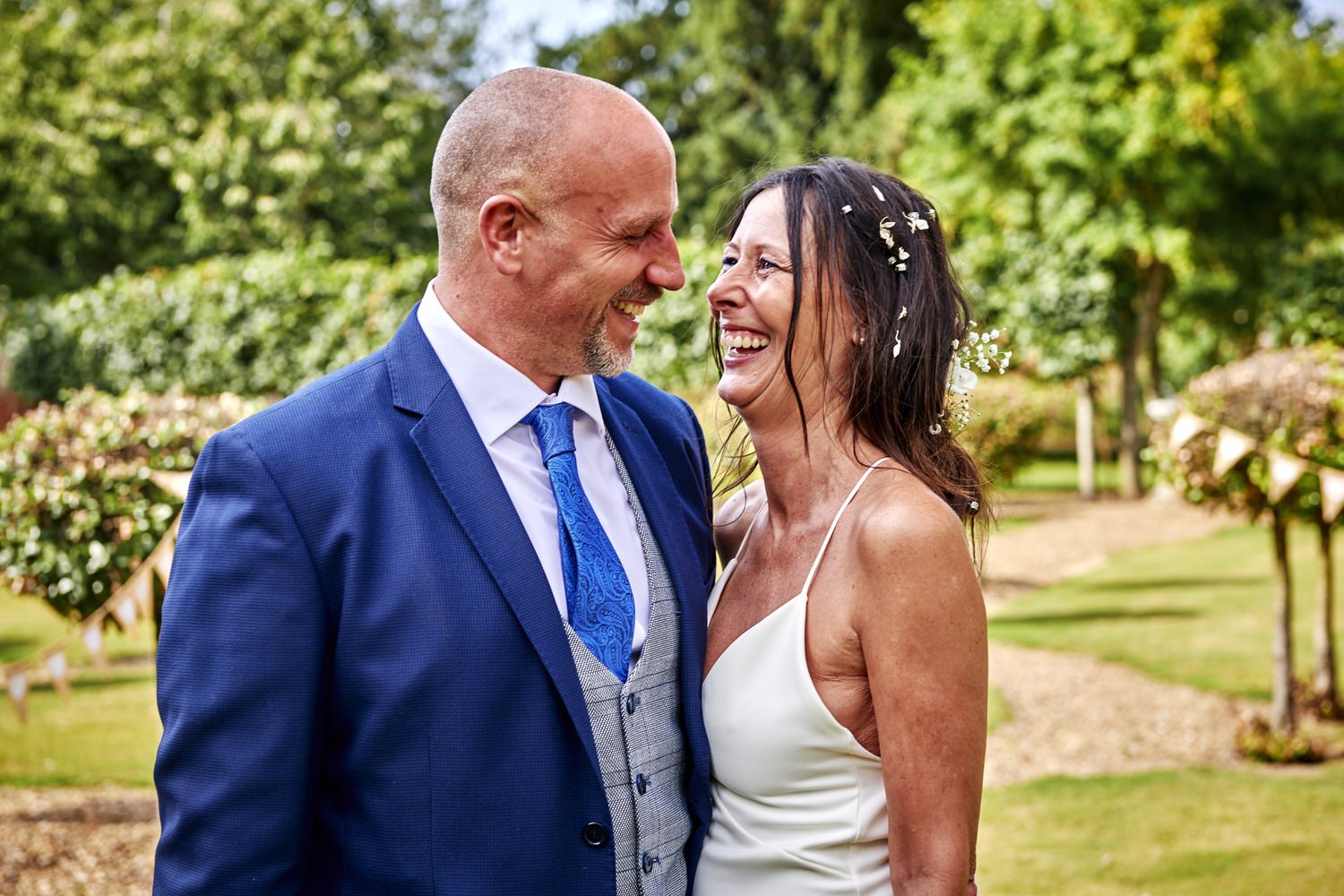 Bride and groom look at each other as they pose in a garden.