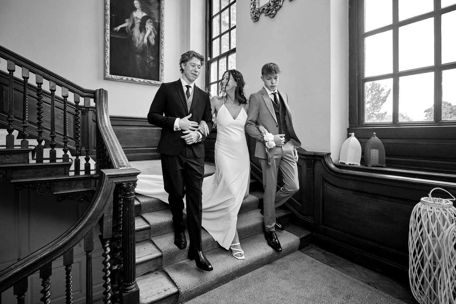 Bride and her two sons walk down a large sweeping staircase – black and white image.