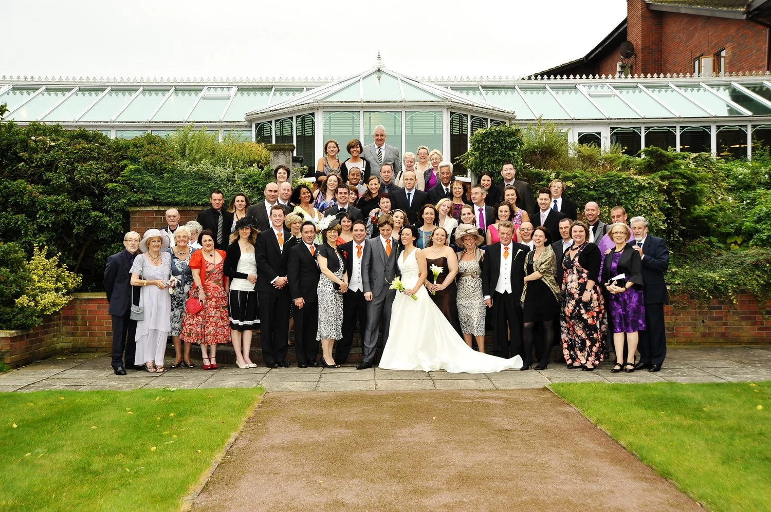Formal group of wedding guests posed before a large glass building.