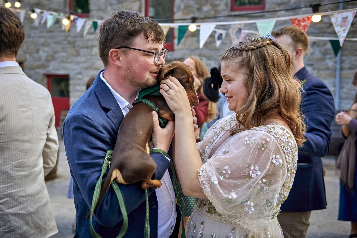 Bride and groom hold their dog in their arms.