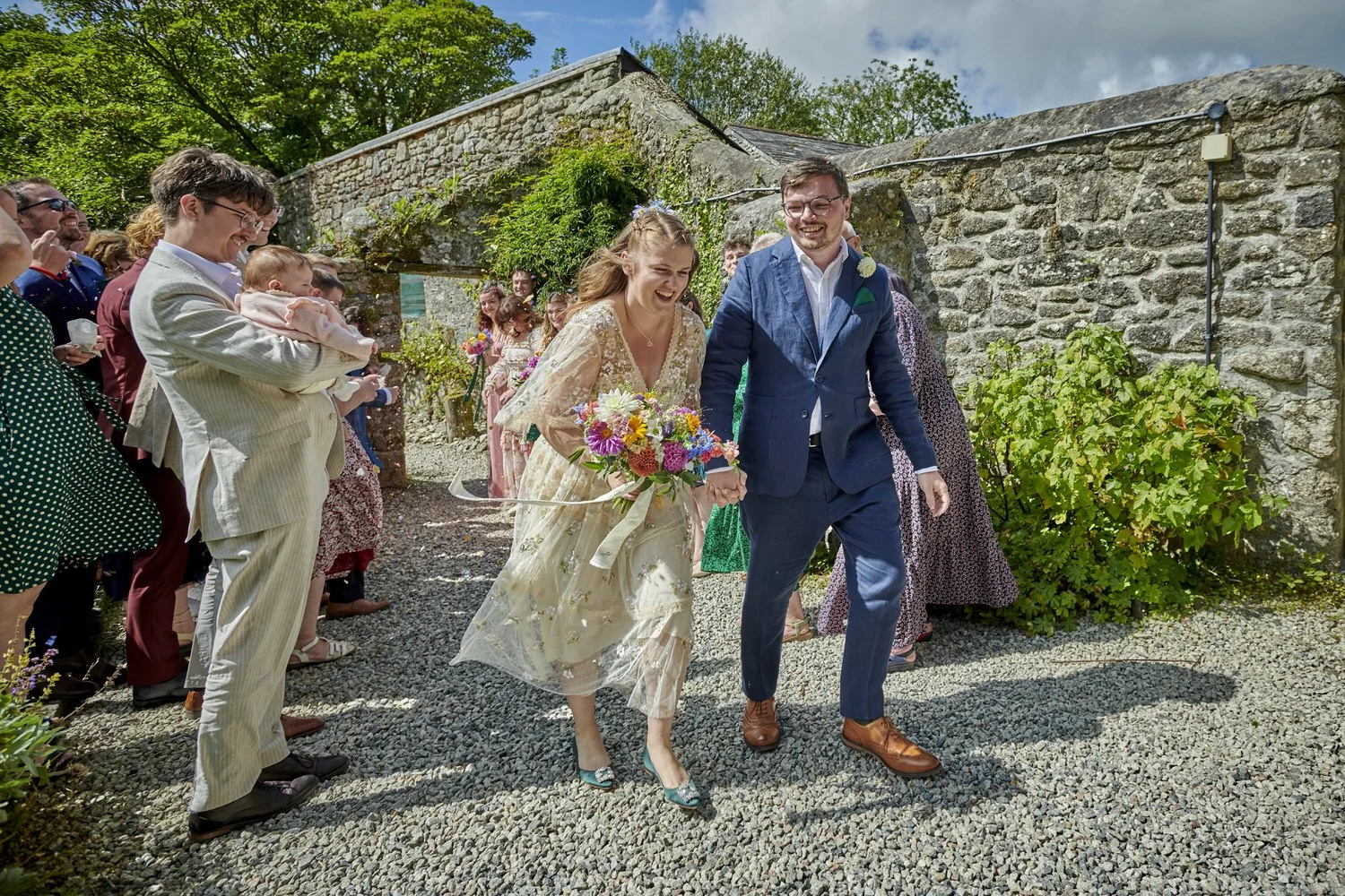 Bride and groom leave crowd of friends and guests covered in confetti.