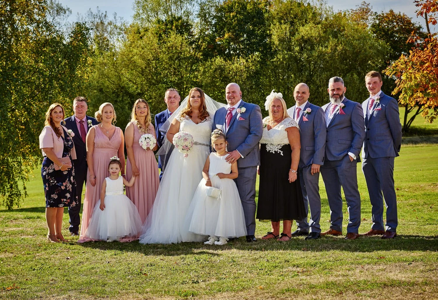 A formal group of friends stand for a photograph in the sun.