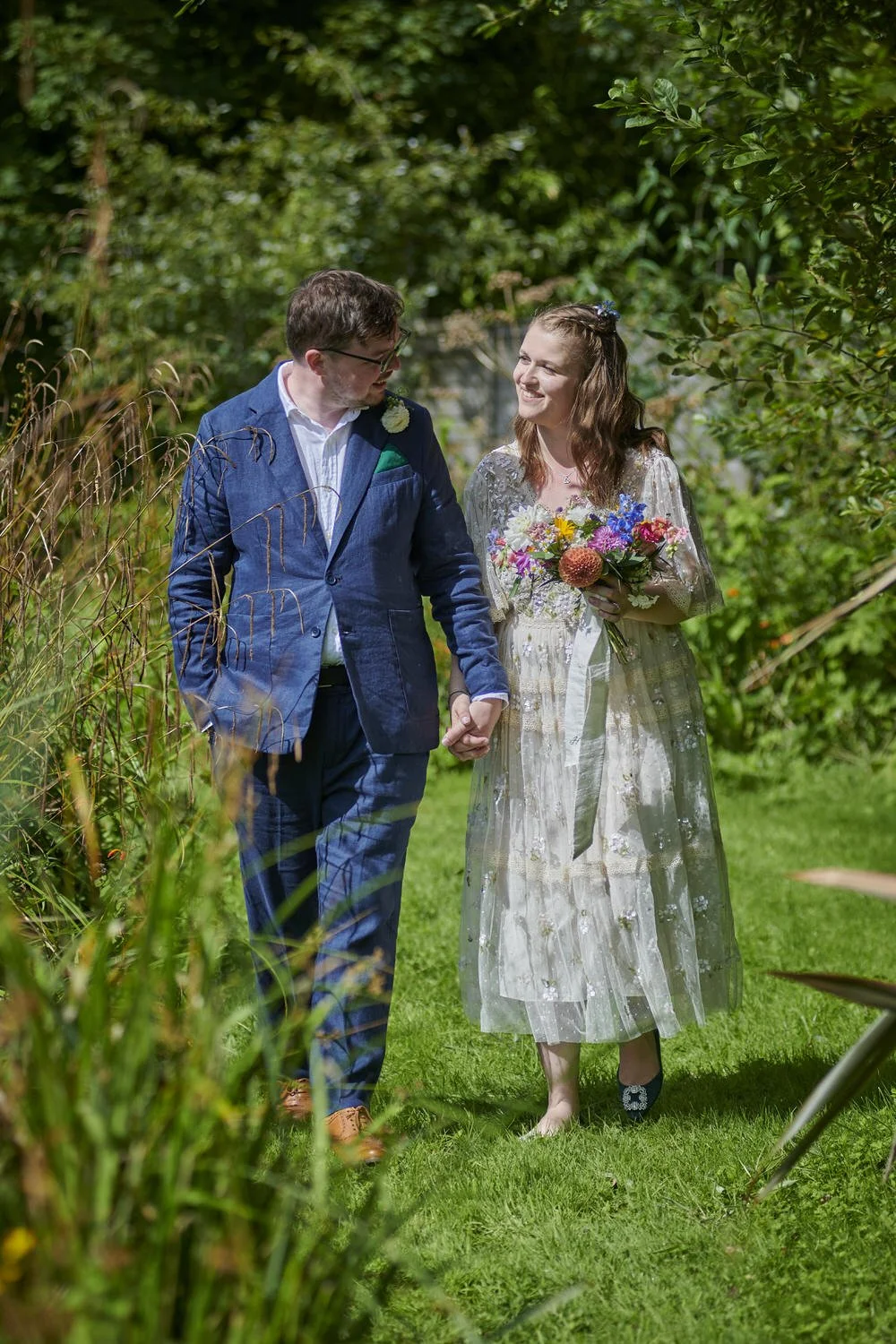 Candid shot of bride and groom walking through flower garden talking to each other.