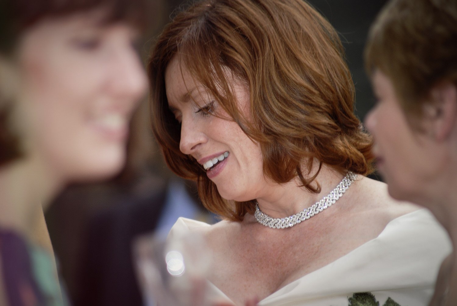 Bride looks at the ground thoughtfully with out of focus friends in the foreground.