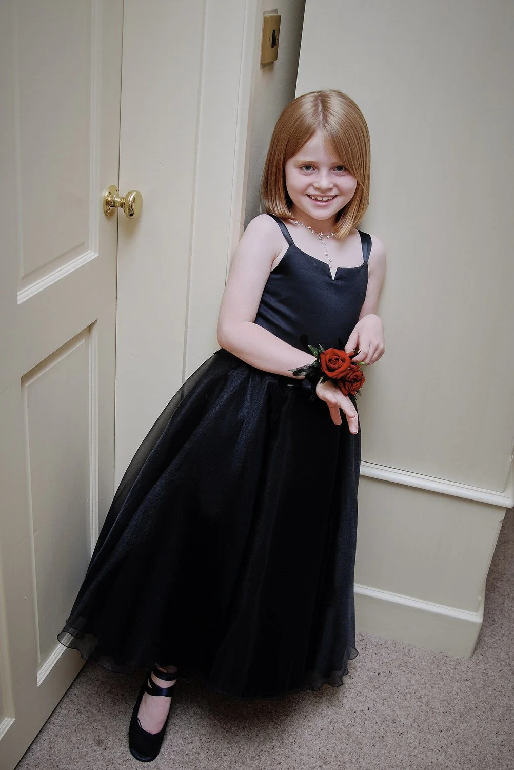 Young bridesmaid in green dress leans against doorframe smiling.