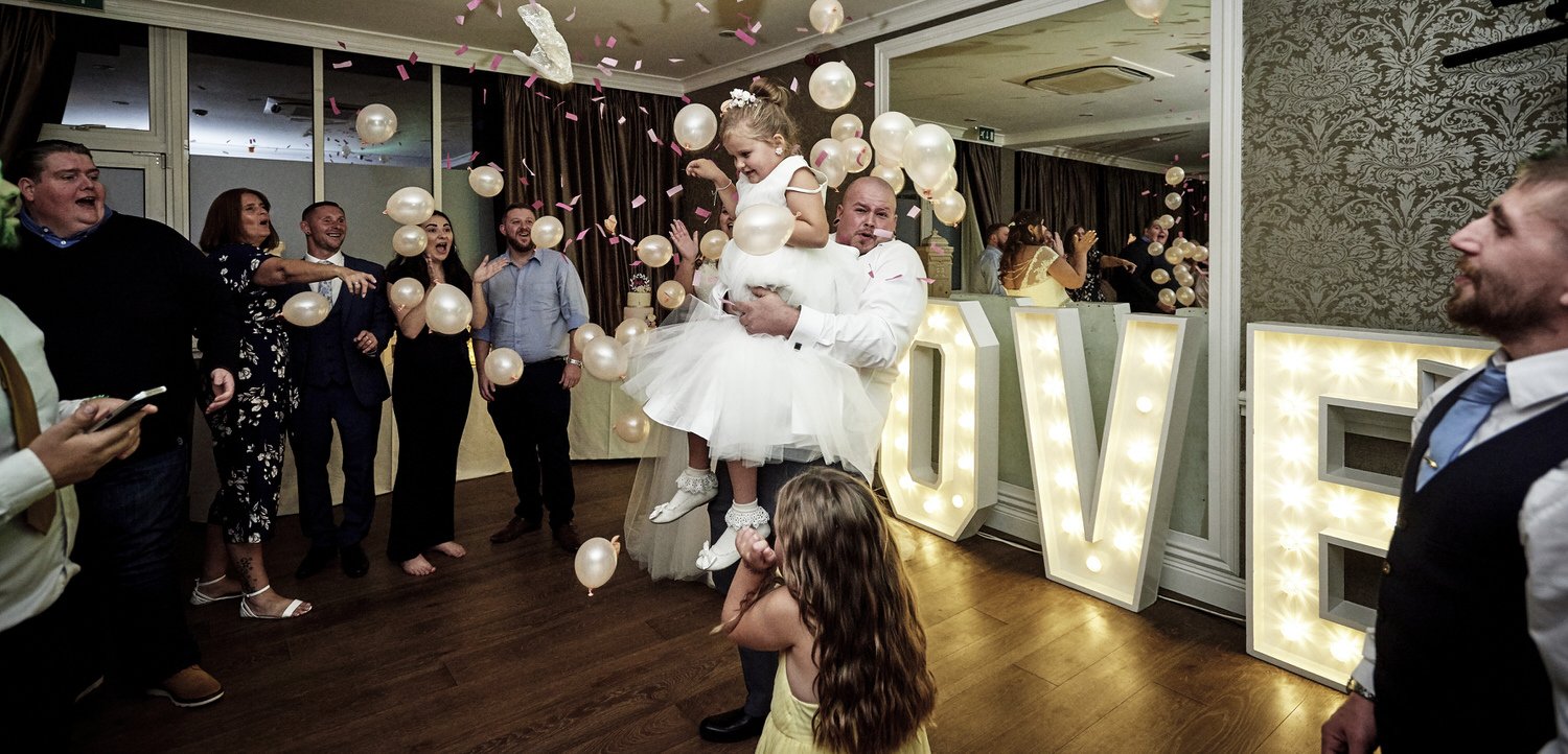 The groom picks up his little daughter to dance with her and the guests watch and smile.