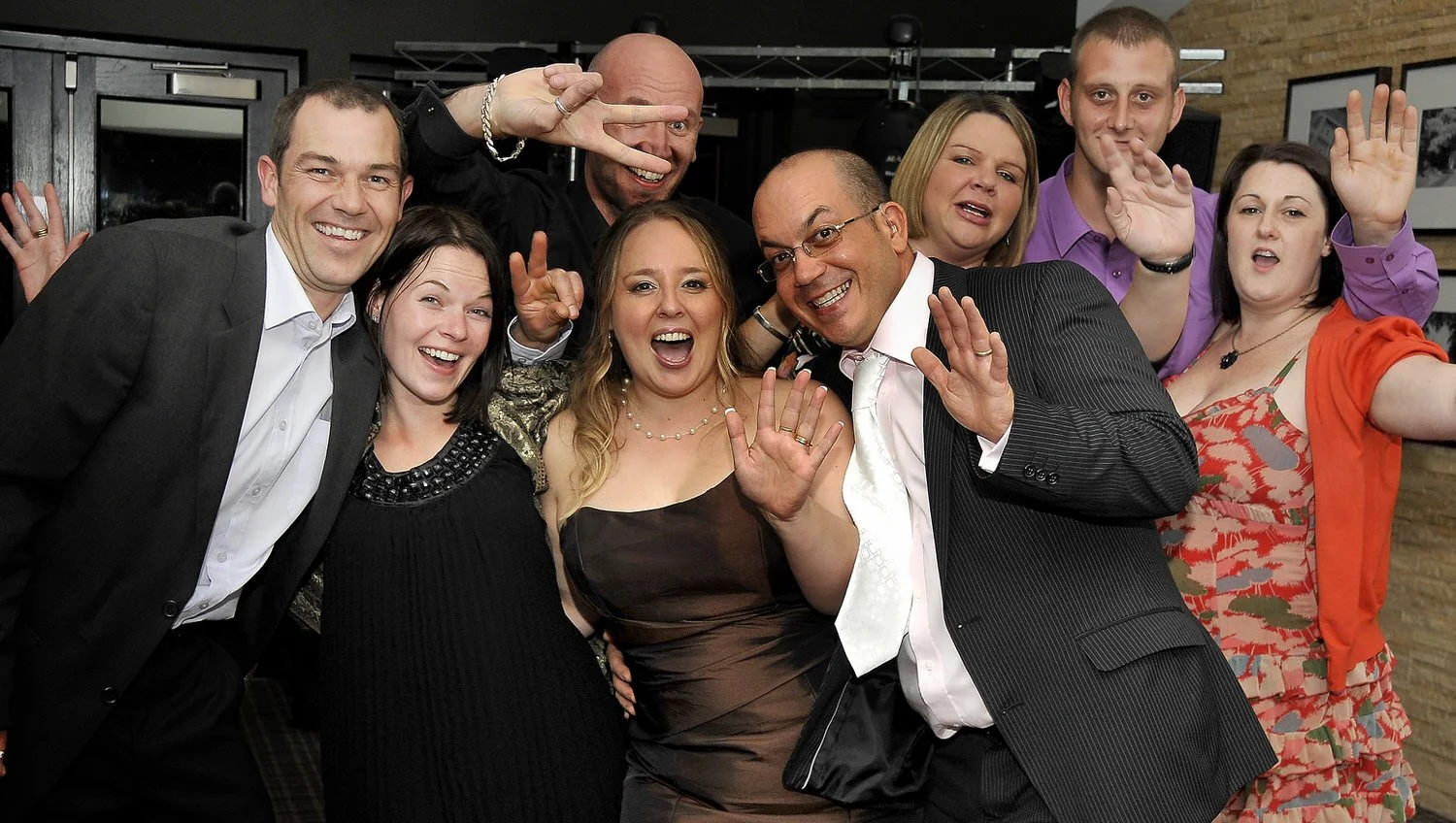 A group of friends gather together and wave at the camera.