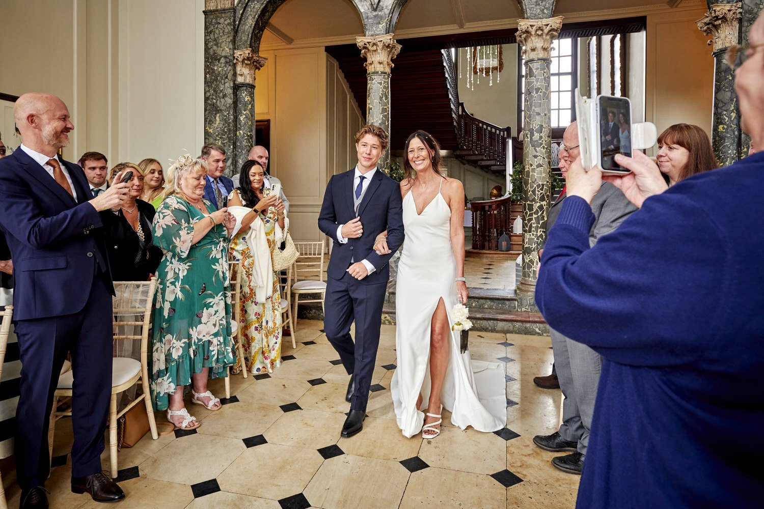 Bride and best man walk down the aisle as guests clap her arrival.