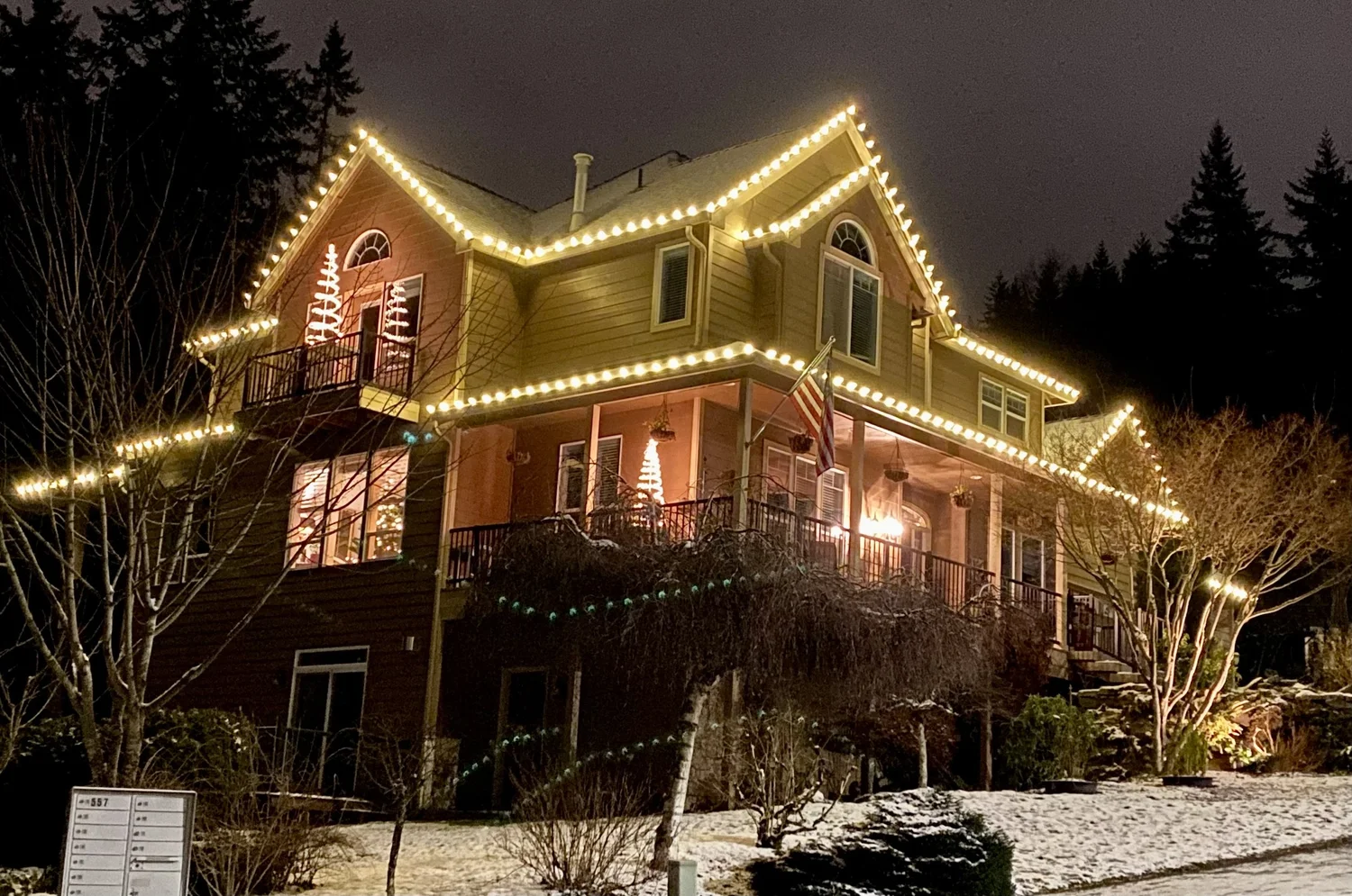 Warm white Christmas lights on a two-story home's rooflines and porch on a snowy evening