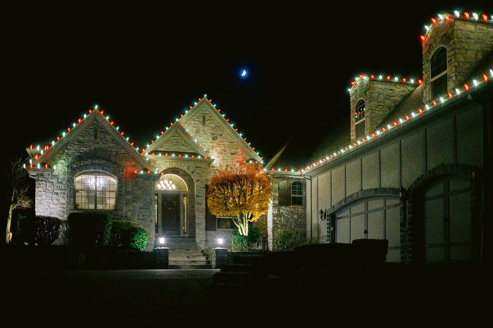 Lit roofline and gables on a stone-front home at night