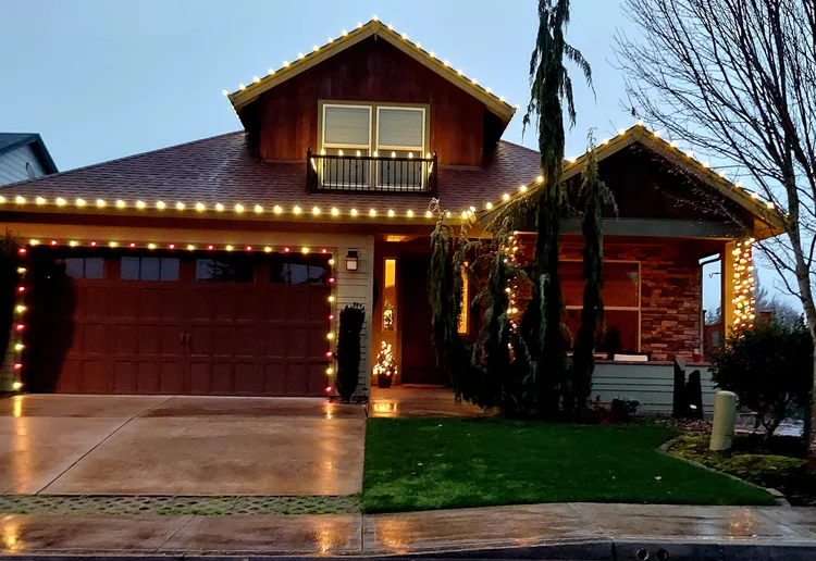 Home with warm white lights on the gables and garage at dusk