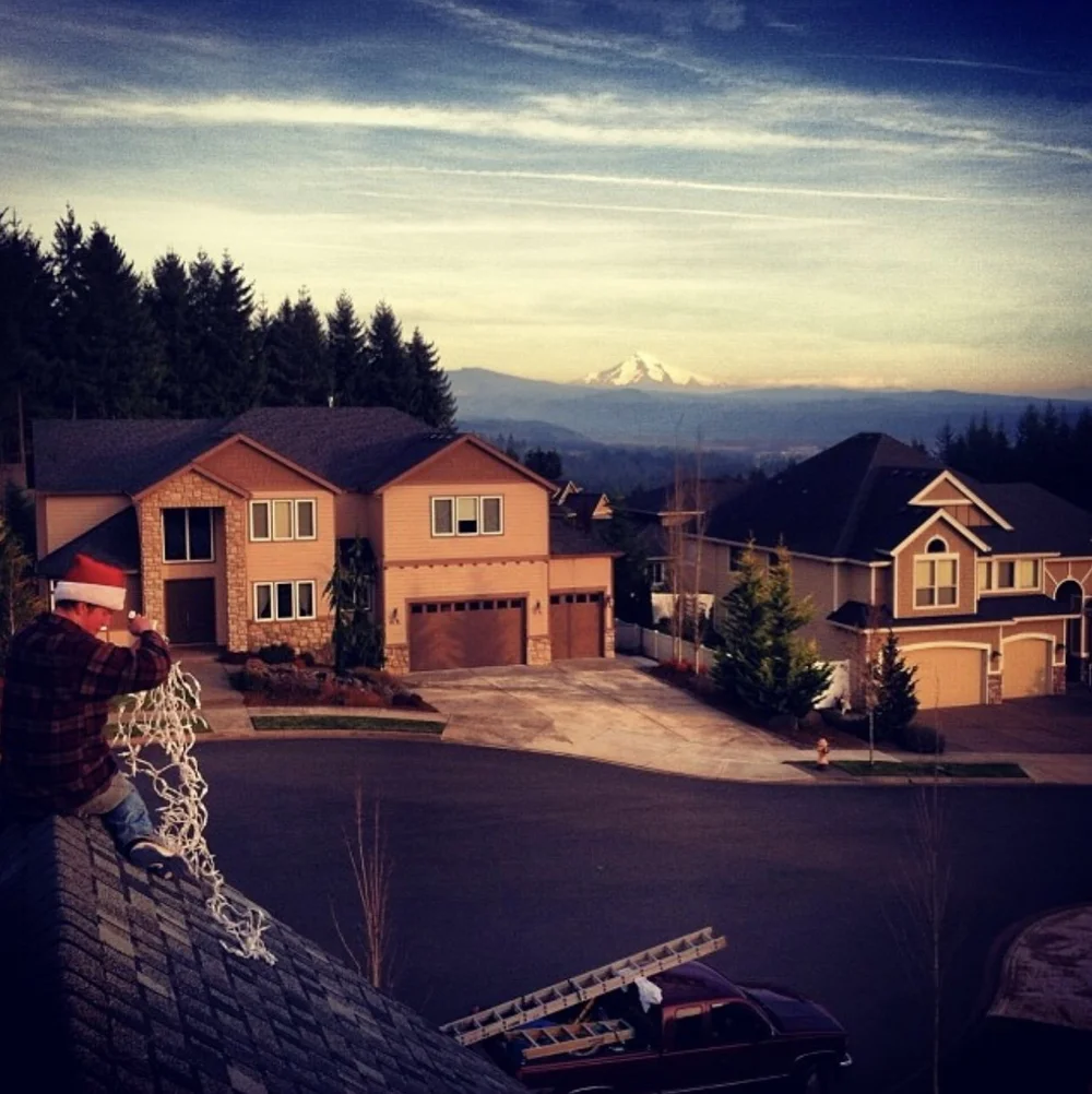 Red Hat installer on a rooftop during a Christmas light install, with a snowcapped peak on the horizon