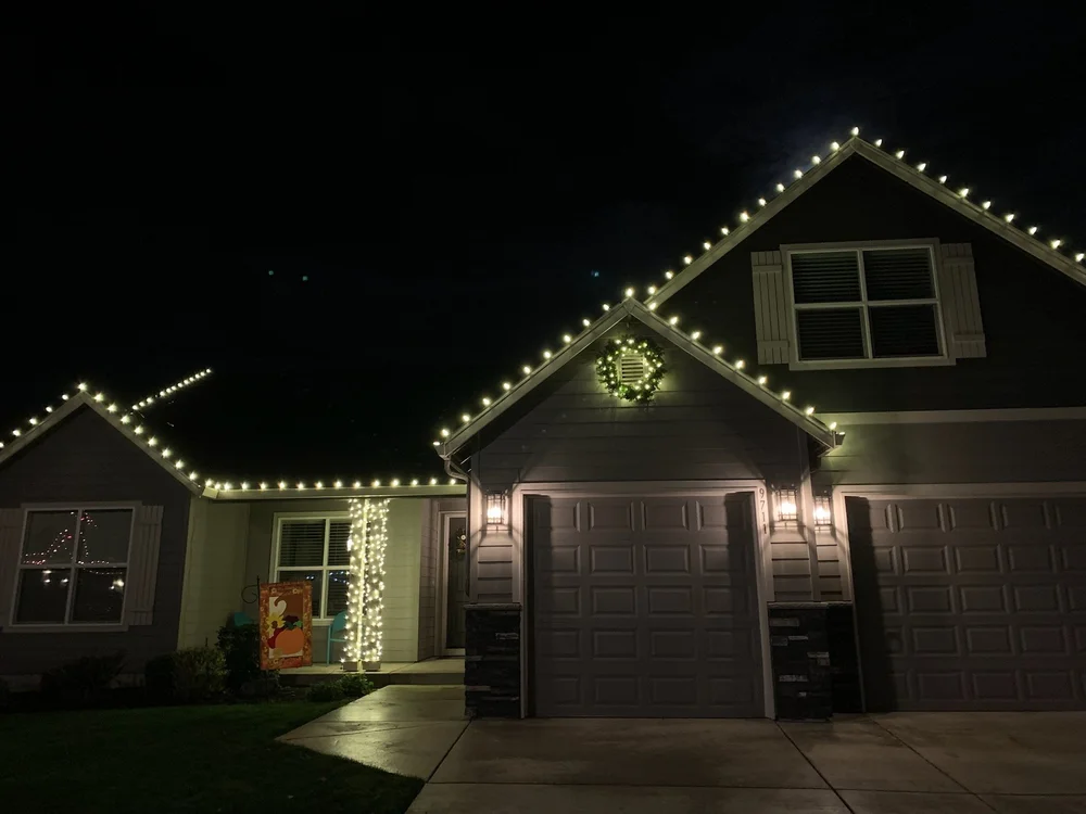 Two-story home with warm white rooflines and a lit wreath on the front gable