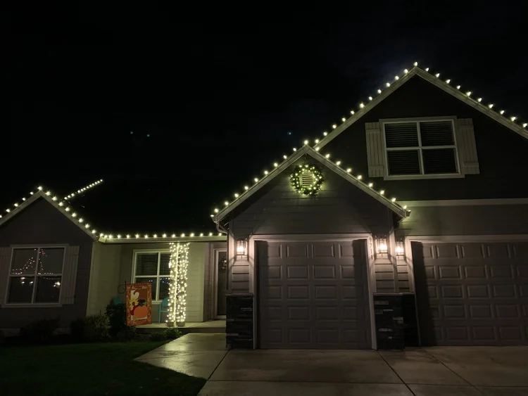 Two-story home with warm white rooflines and a lit wreath on the front gable
