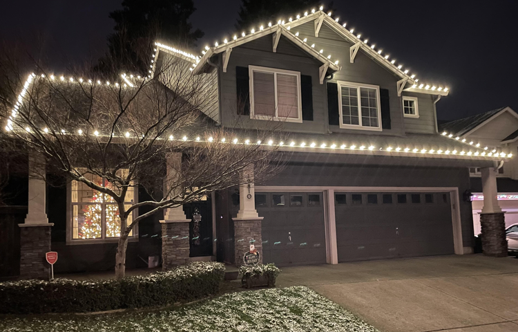 Two-story home with faceted warm white bulbs along every roofline and a light dusting of snow