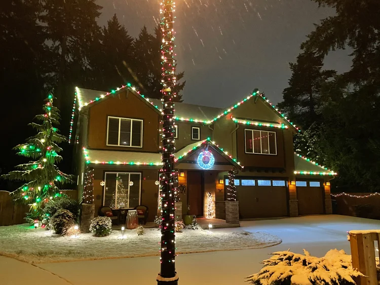 Snow-covered home with red, white and green lights and a lit tree in the yard