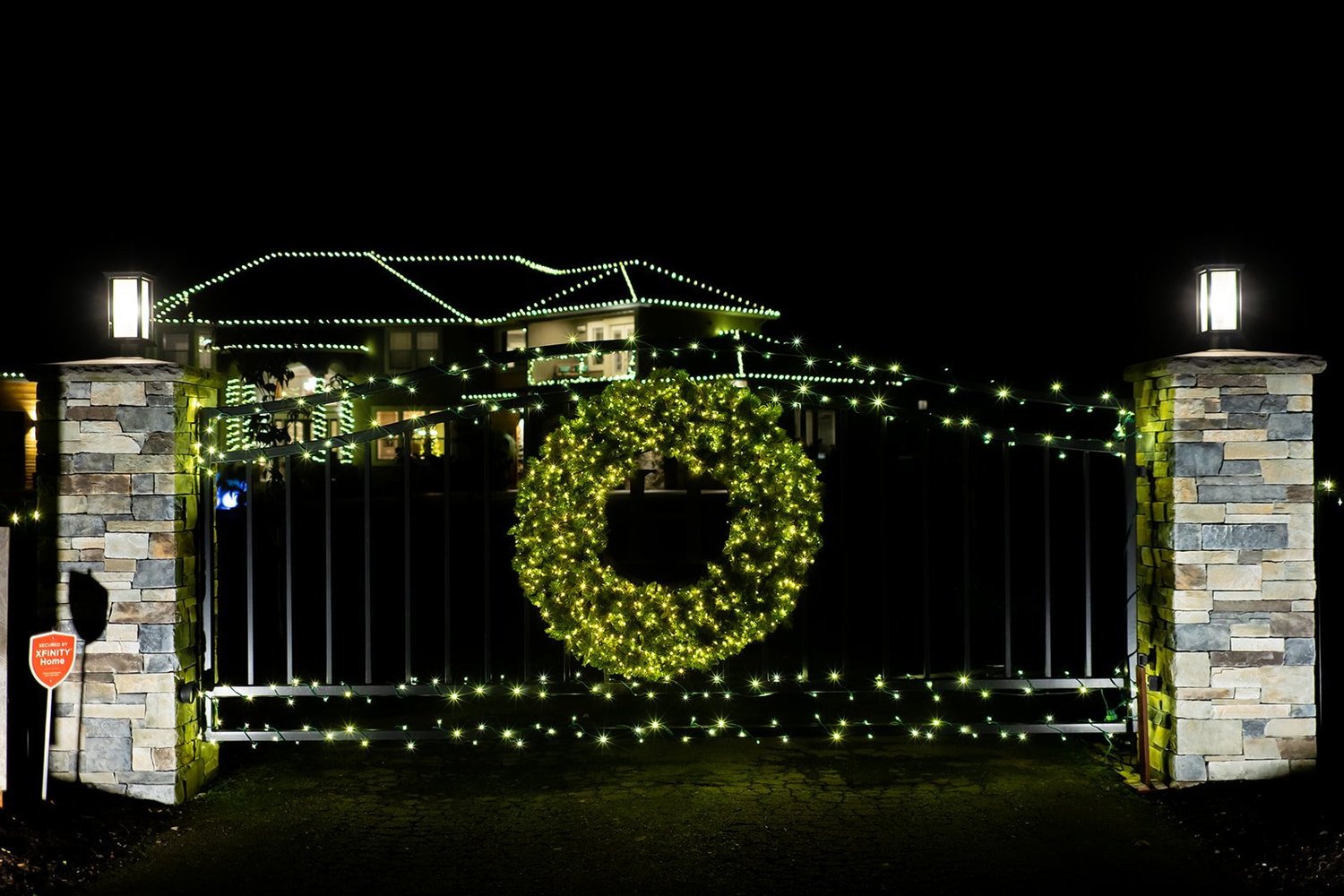 Gated entry with a lit wreath and mini lights along the fence and stone pillars