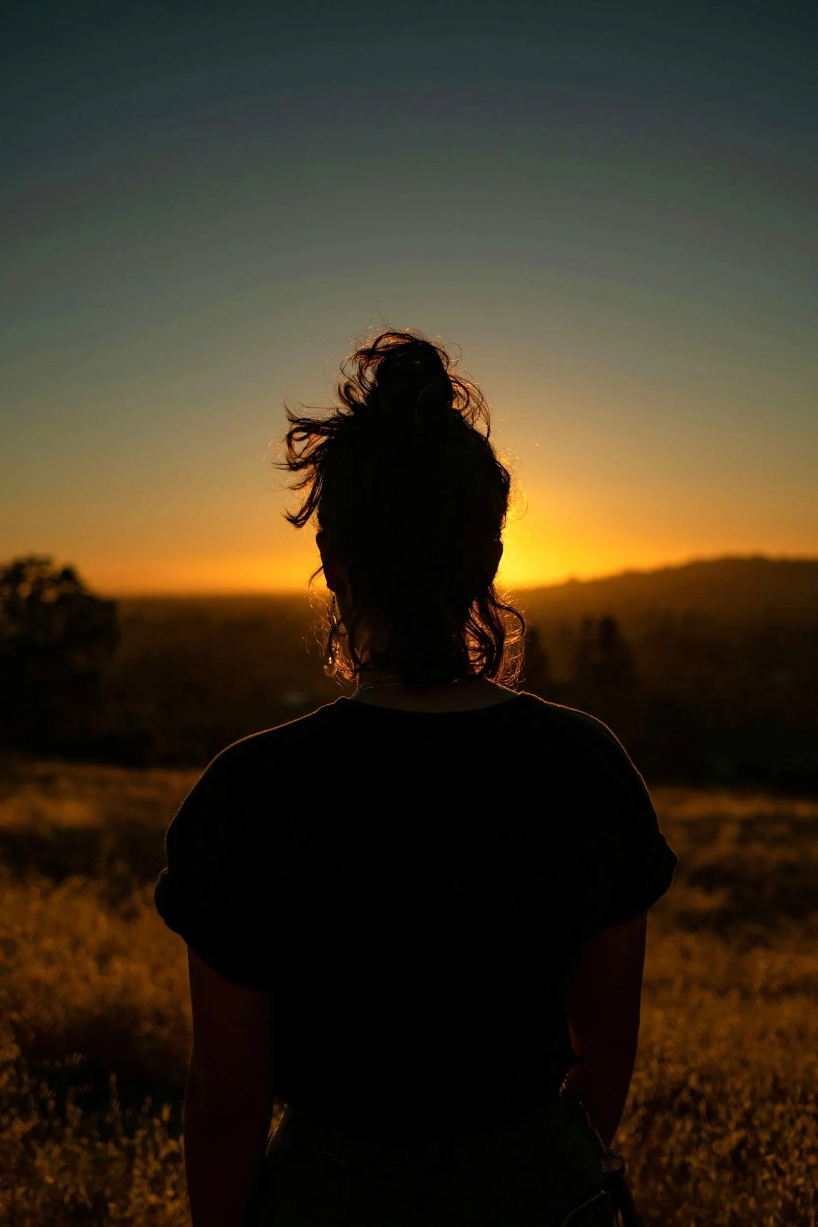 Woman silhouette seen from behind against the golden horizon at sunset