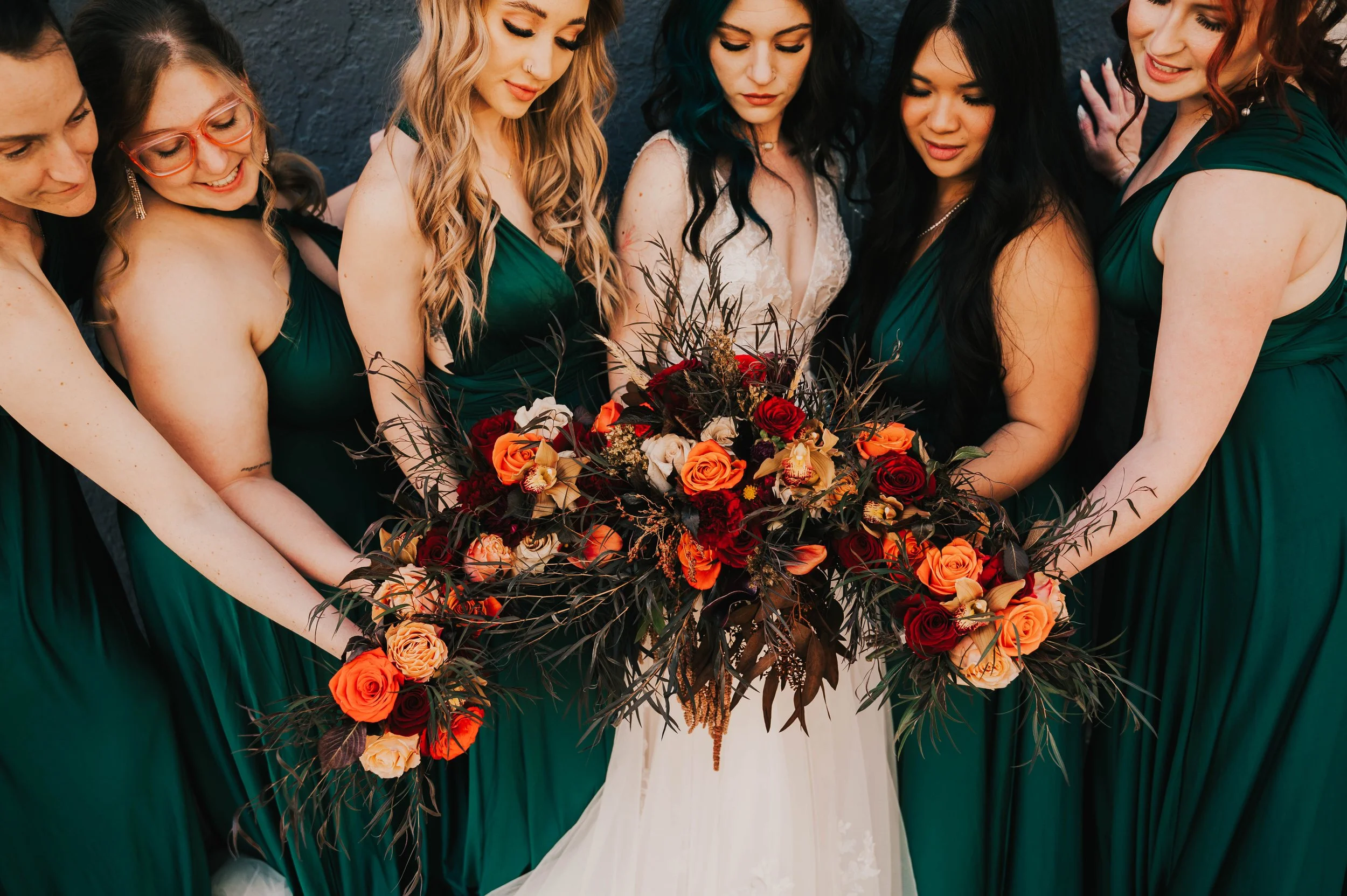 Group of women in green dresses and bride in white dress holding a large floral bouquet