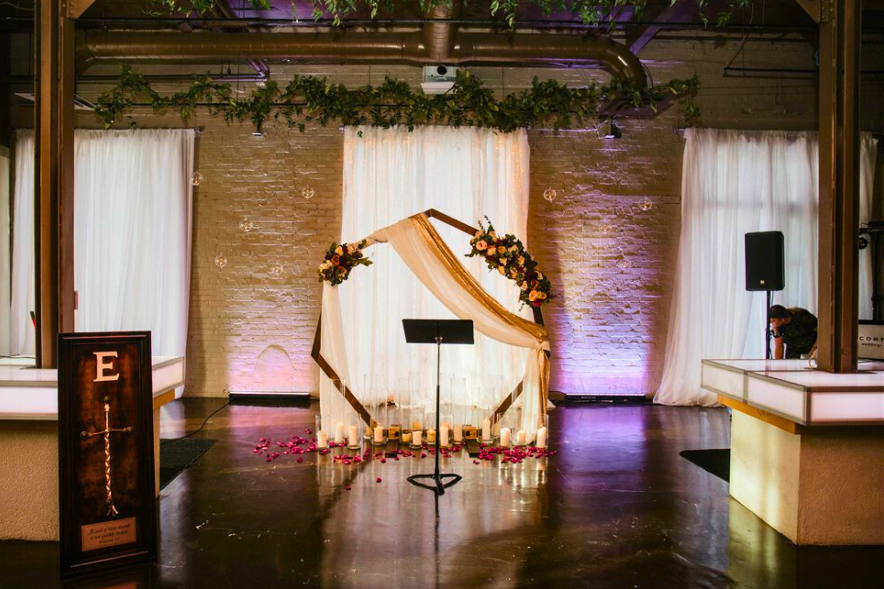 Wedding altar with floral decorations, candles, and flowing drapes in a decorated indoor venue.