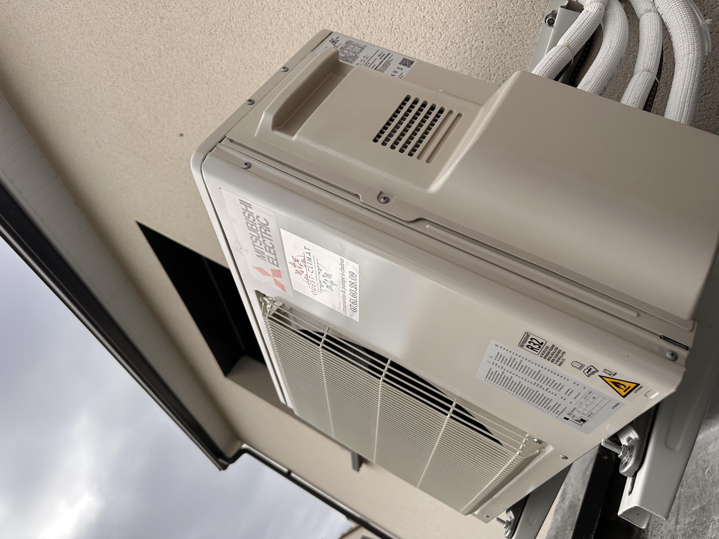 climatisation Mitsubishi Electric installé à l'extérieur d'un bâtiment, fixé au mur.