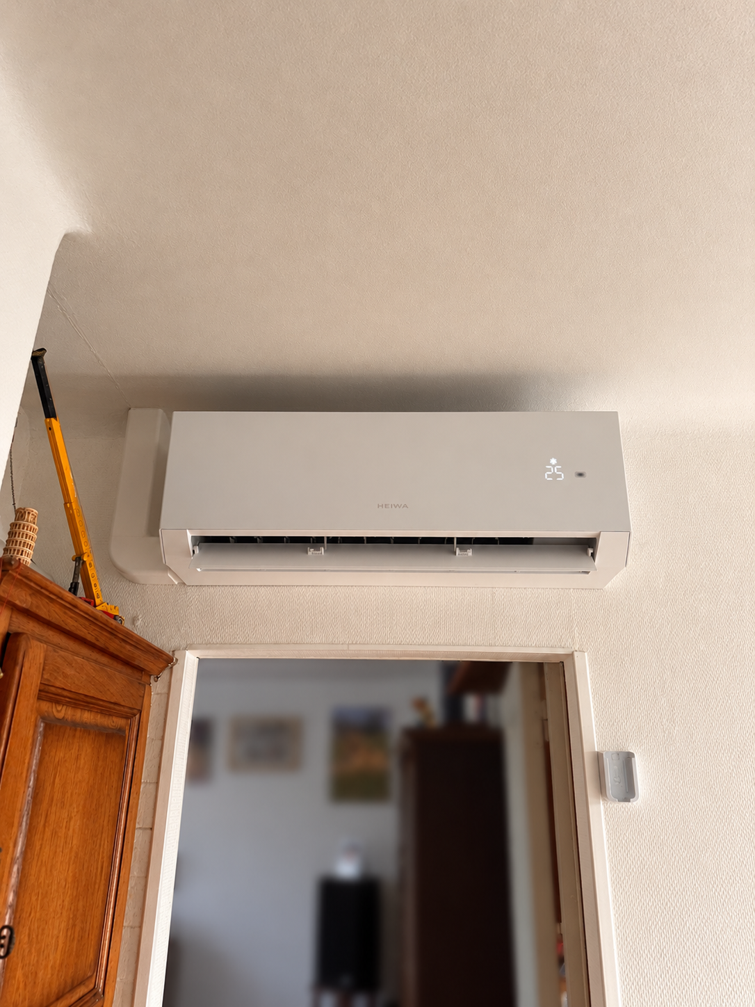 Climatiseur blanc fixé au mur au-dessus d'une porte, affichant la température de 25°C.
