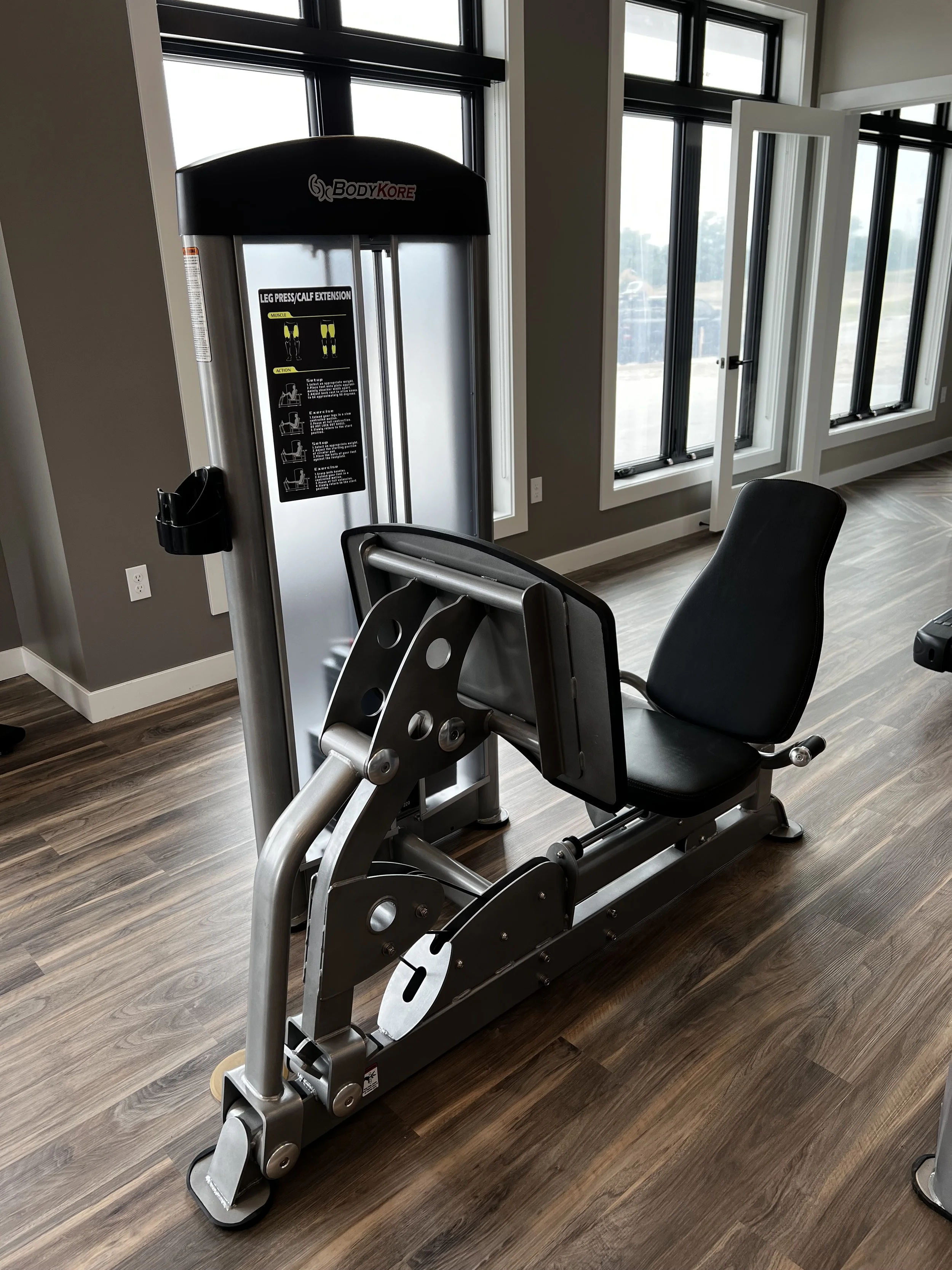 A gym machine designed for leg press and calf extension exercises in a bright room with large windows.