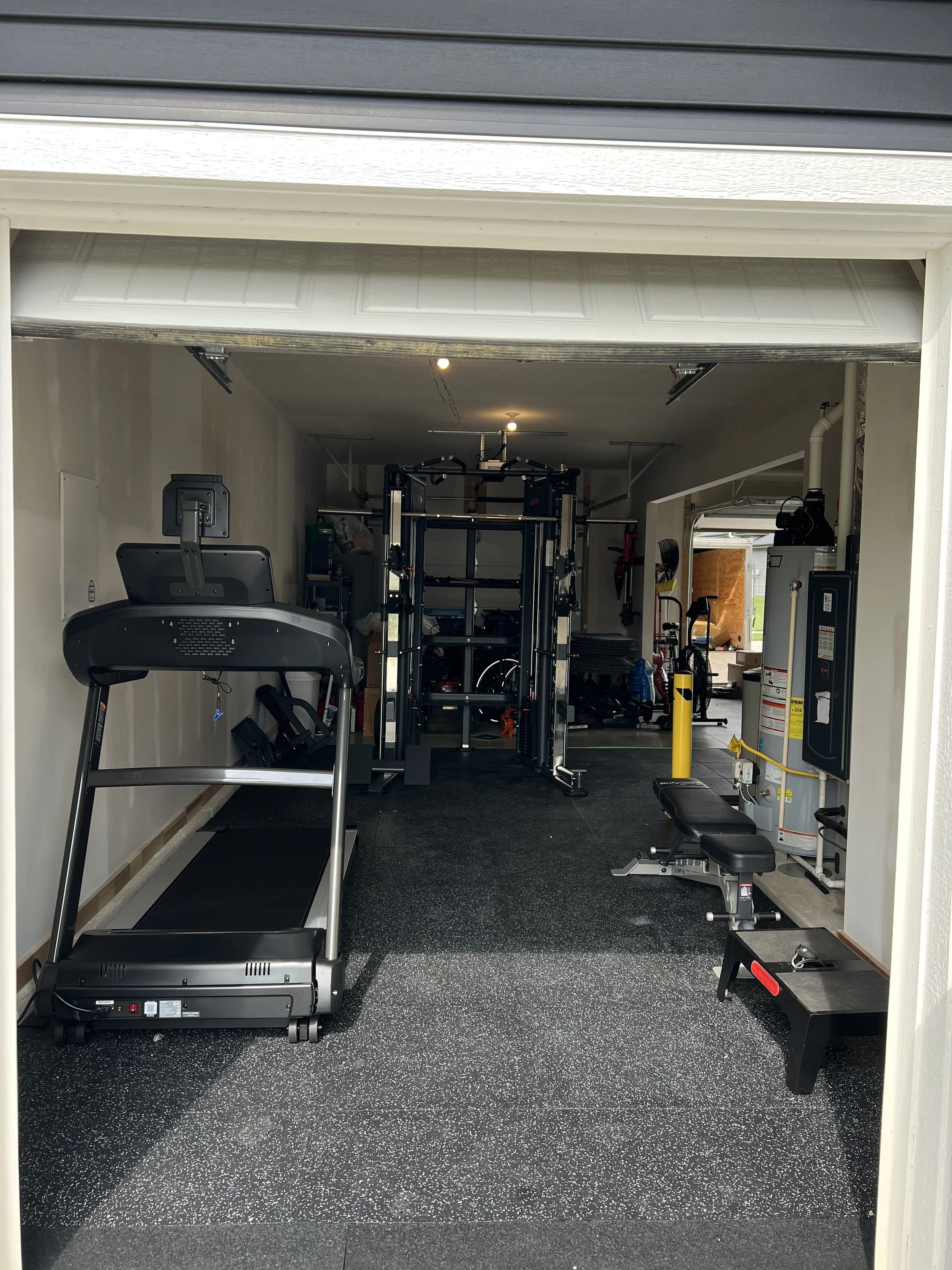 Garage gym with treadmill, weightlifting equipment, bench, and various exercise gear.