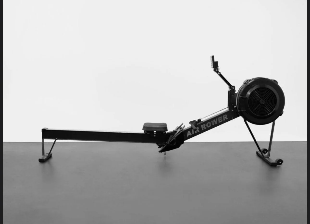 A black rowing machine on a gray floor against a plain white wall.