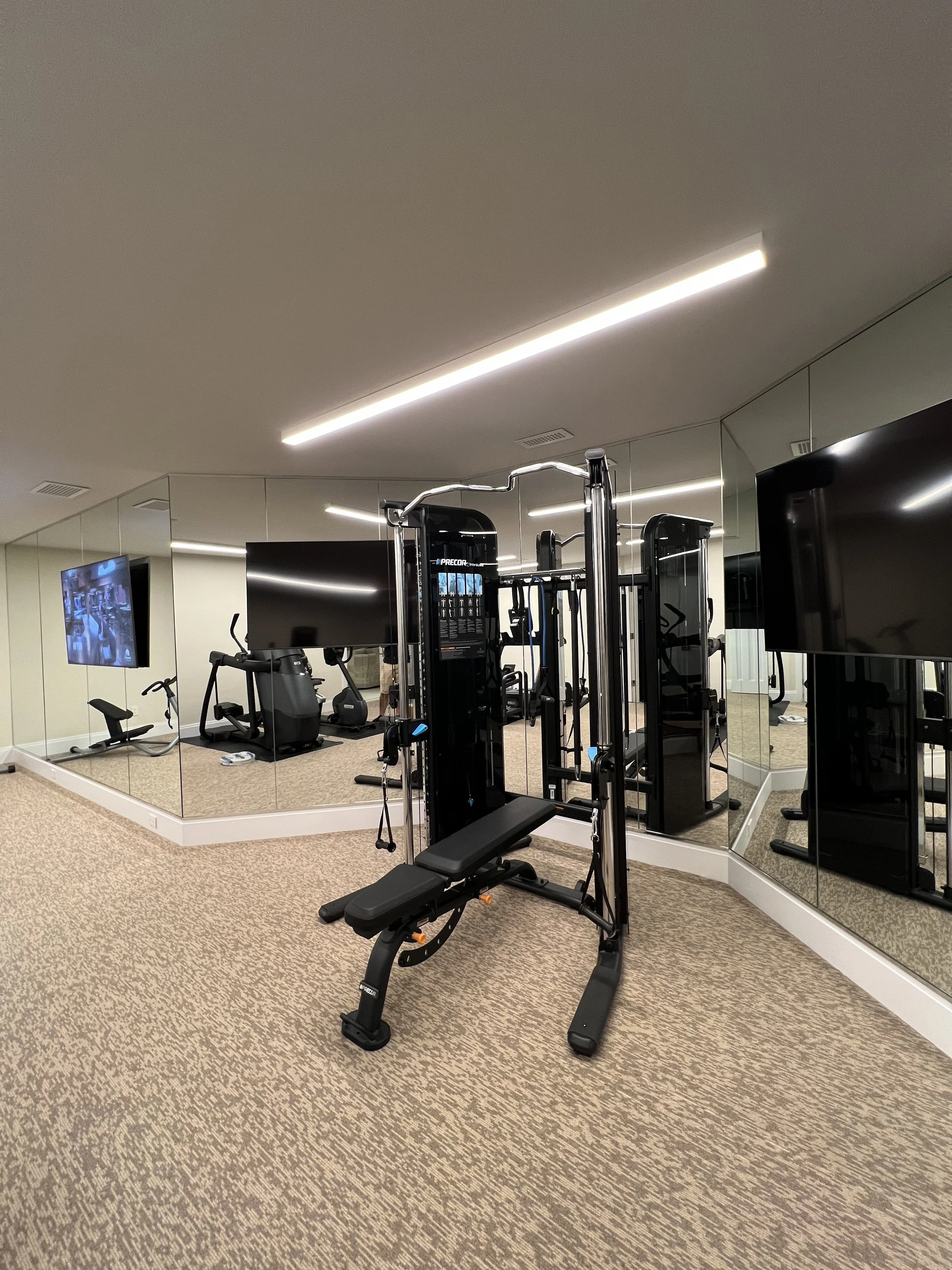 Home gym with a multi-purpose weight machine, a stationary bike, a treadmill, a TV, and a large mirror on the wall.