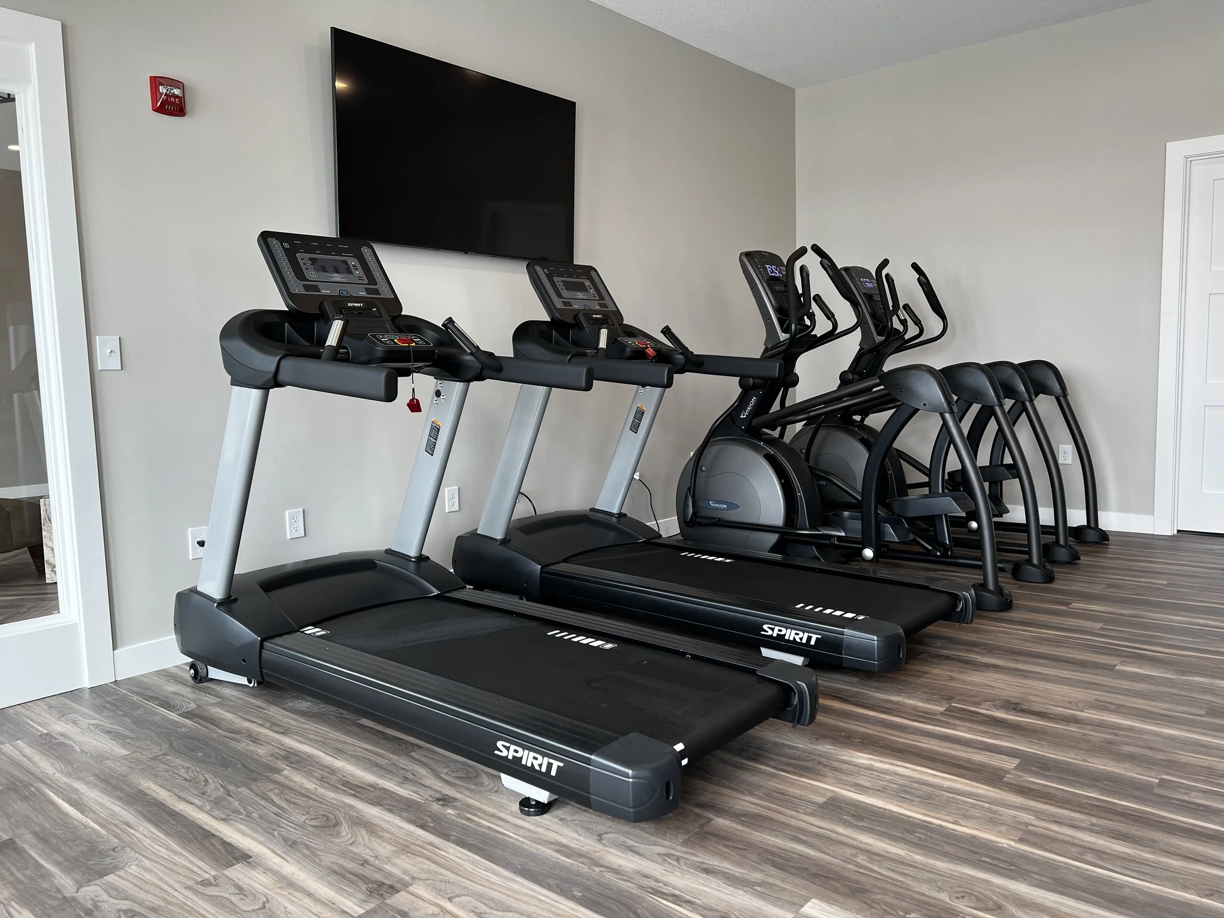 Fitness room with two treadmills, three ellipticals, and a wall-mounted TV.