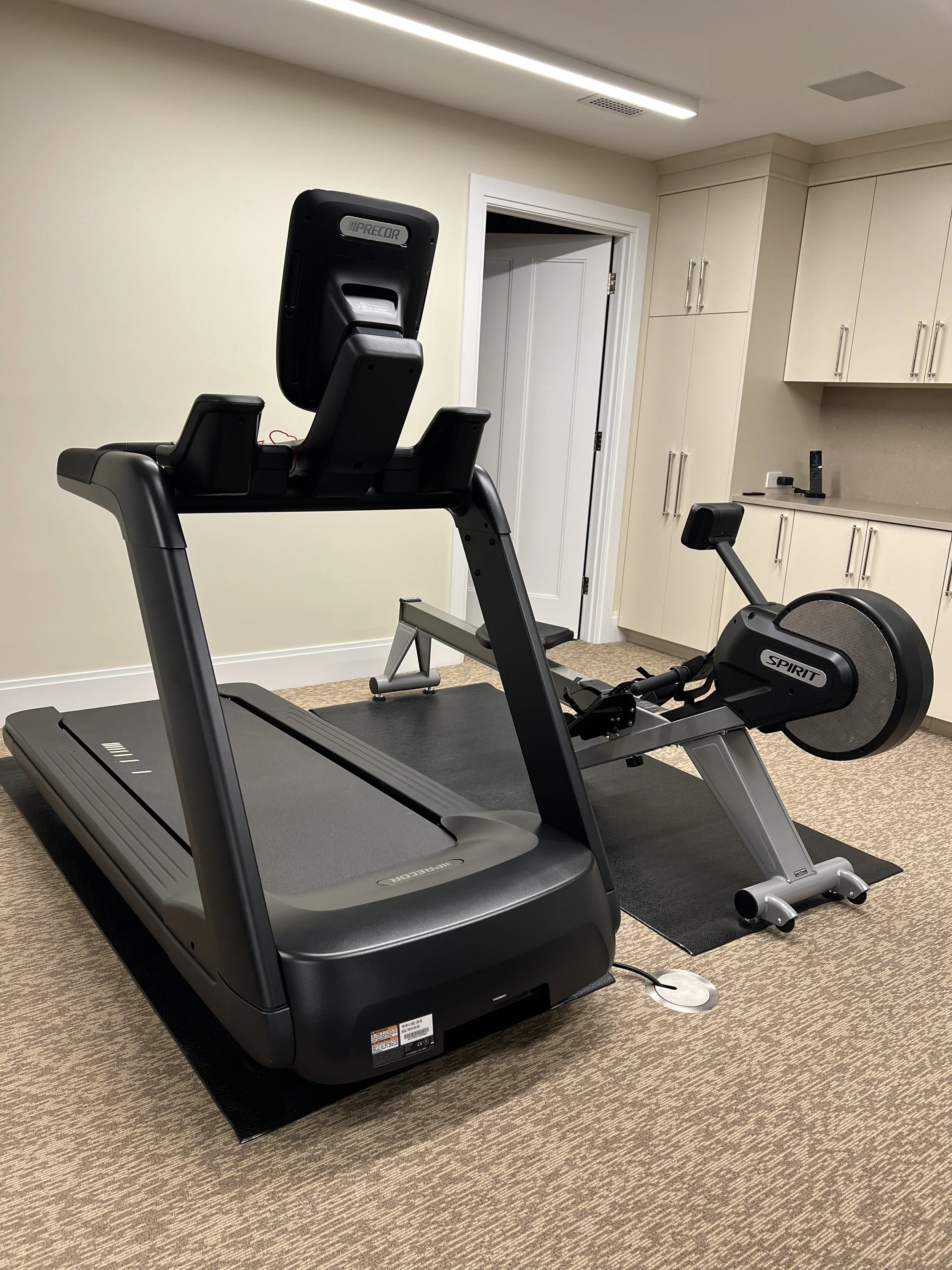 Home gym with a treadmill and a stationary bike in a room with beige walls, cabinetry, and carpeted floor.
