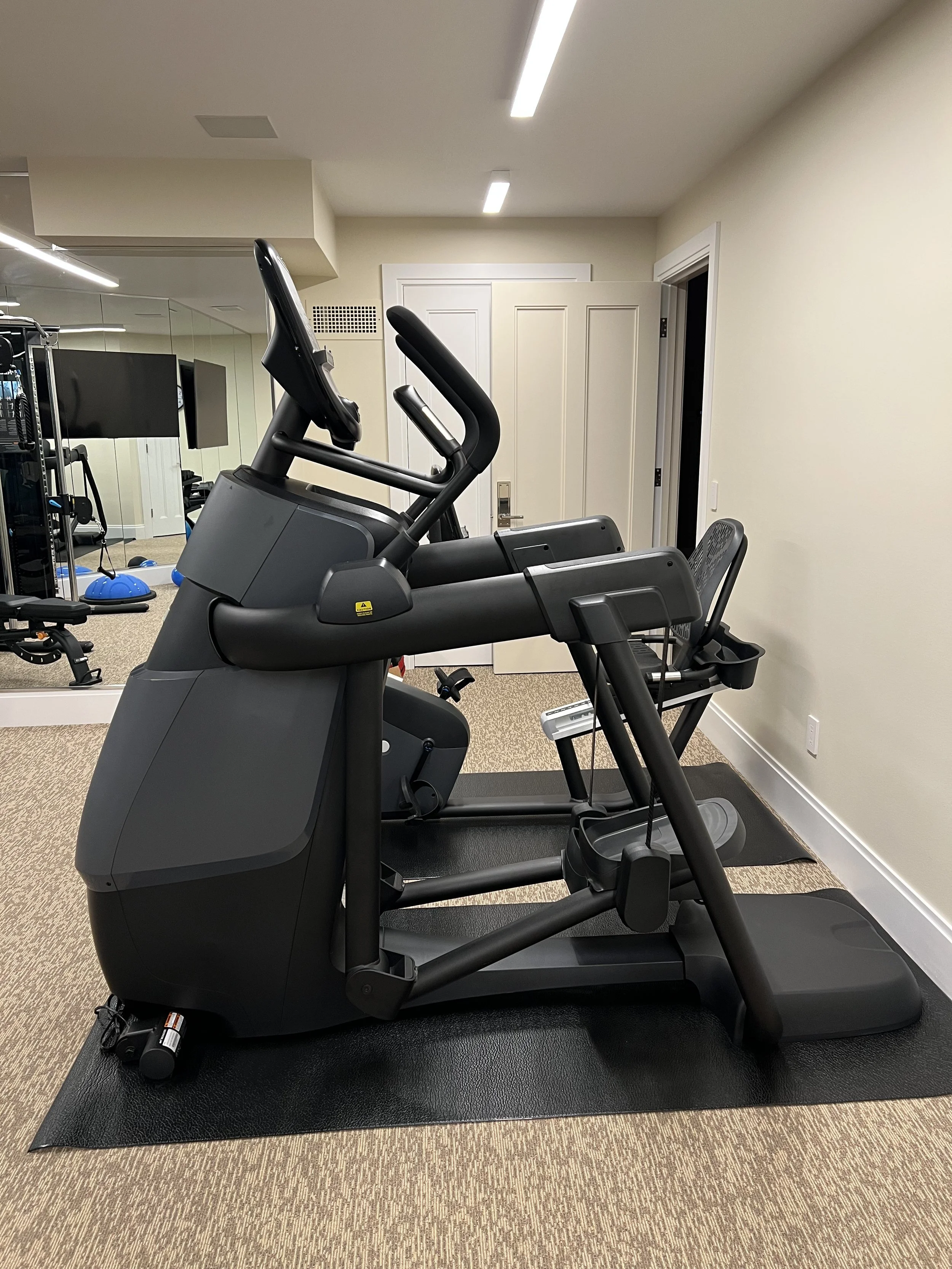 Exercise bike in a home gym with mirrors and a television in the background.