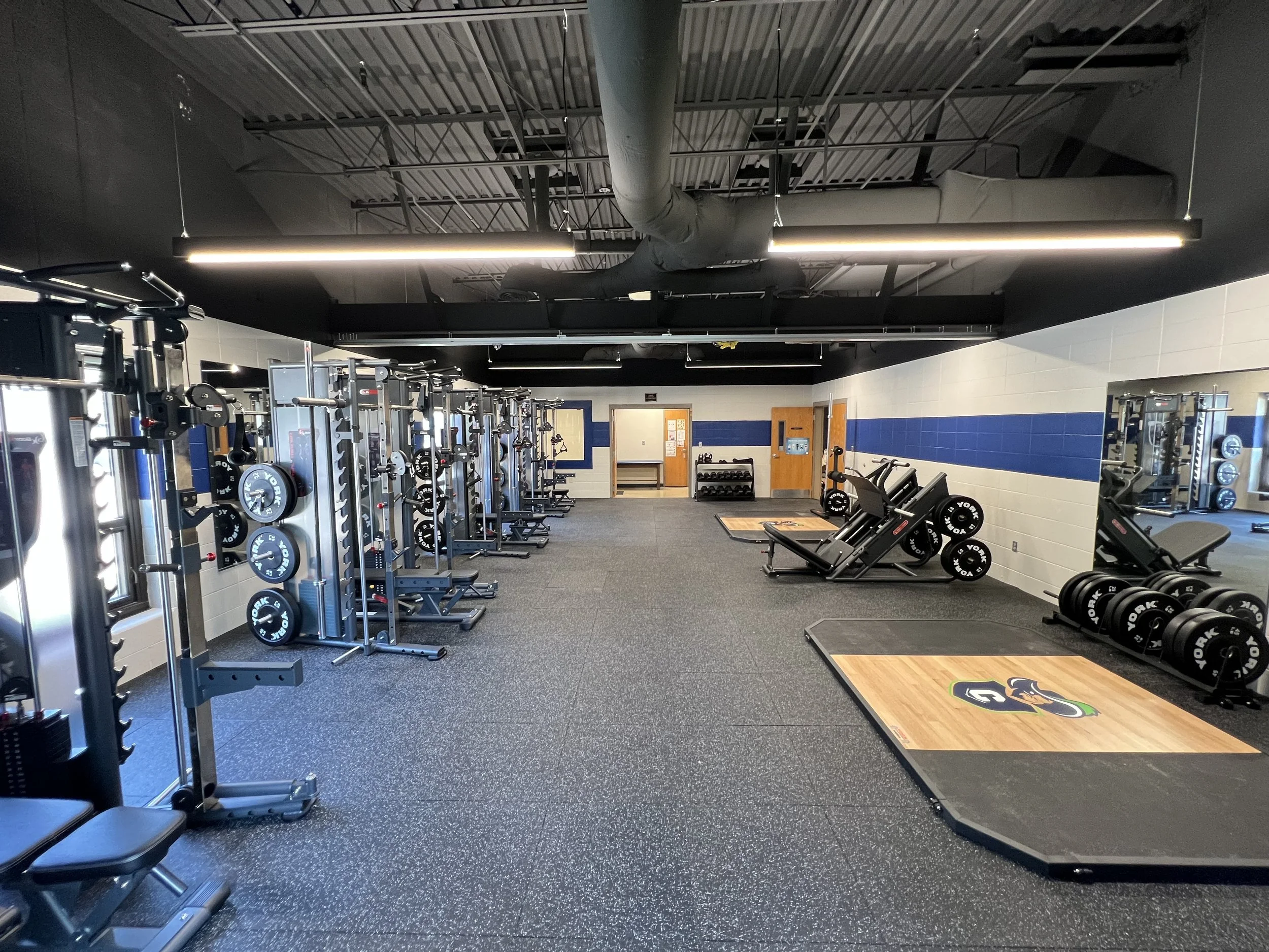 Empty gym with strength training equipment, weight racks, barbells, and weightlifting platforms.