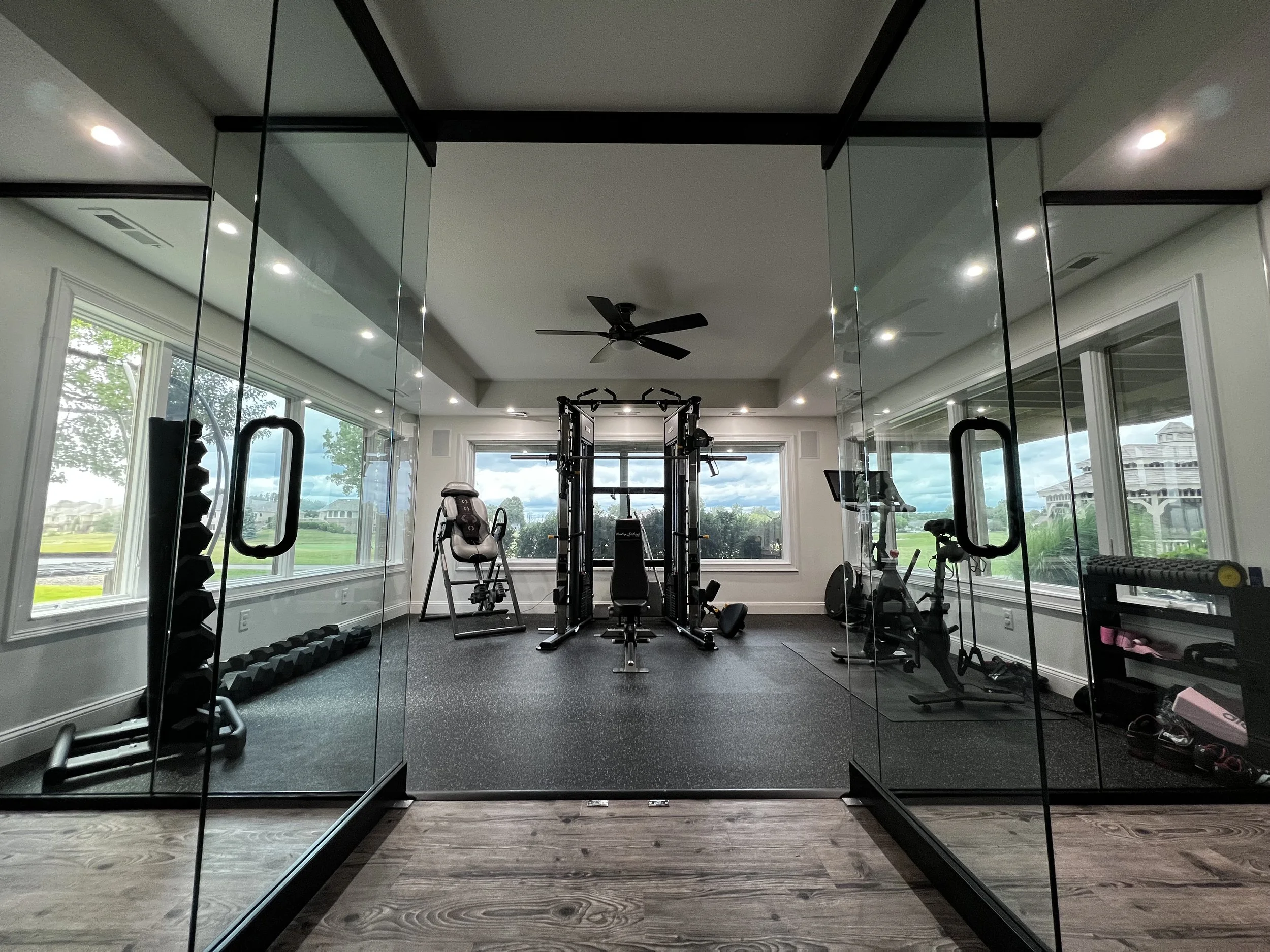 Home gym with large windows, black exercise equipment, and mirrors.