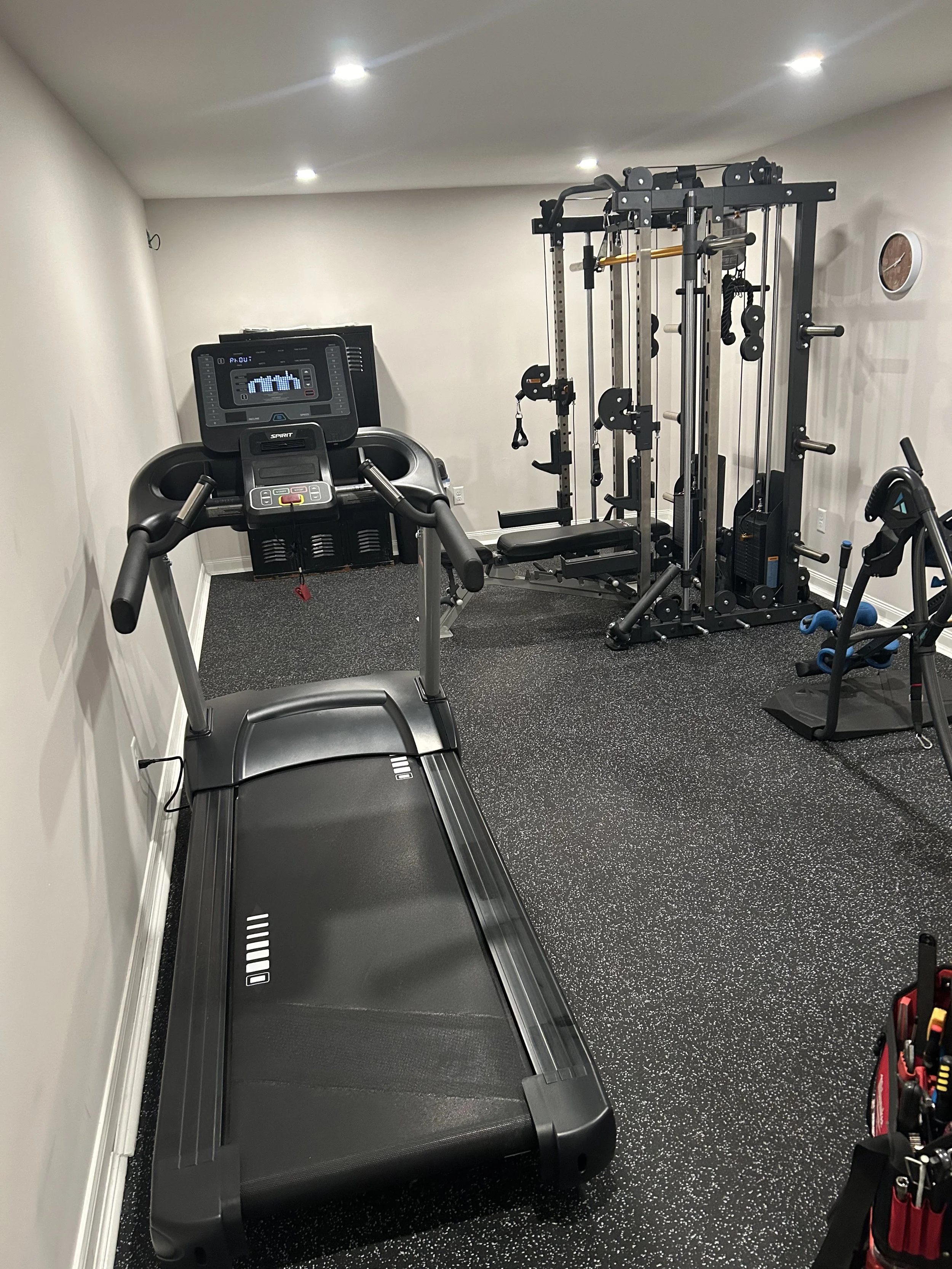 Home gym with treadmill, multi-functional workout station, and small weight area with dumbbells.
