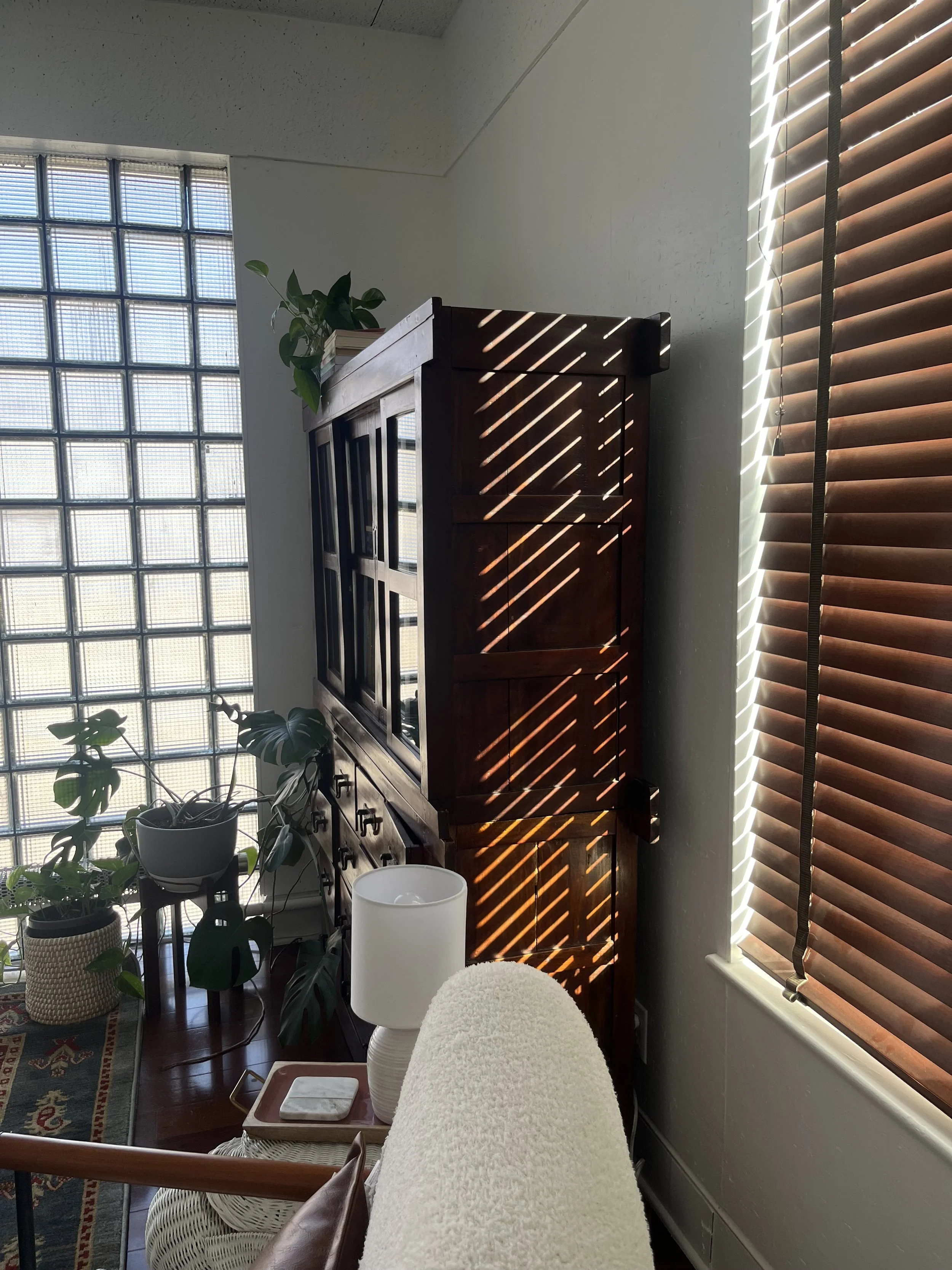 Sunlight filtering through wooden blinds, casting striped shadows on a wooden cabinet in a cozy living room.