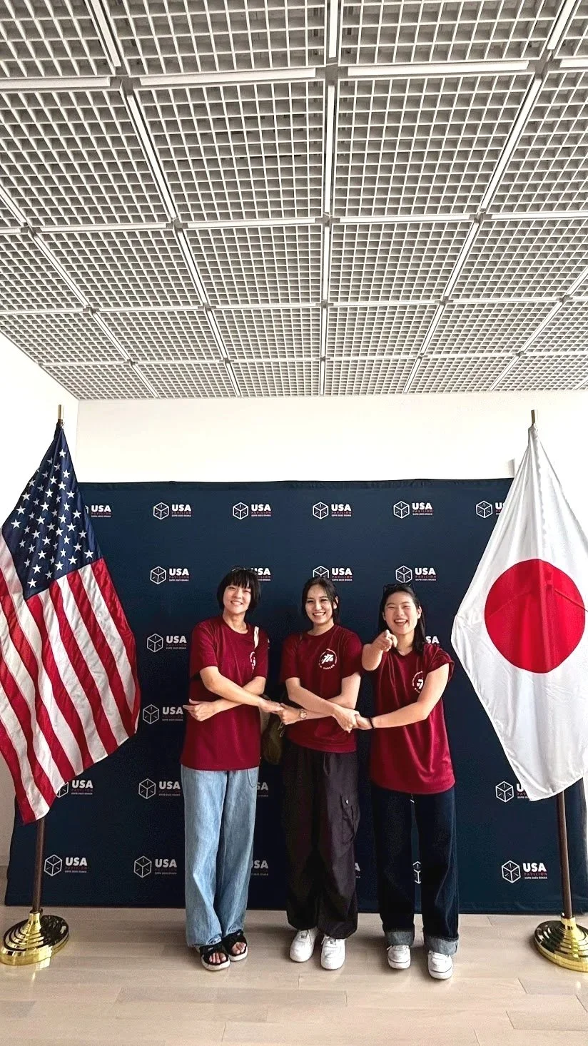 Three JASC delegates standing between American and Japanese flags, celebrating international friendship and student diplomacy.