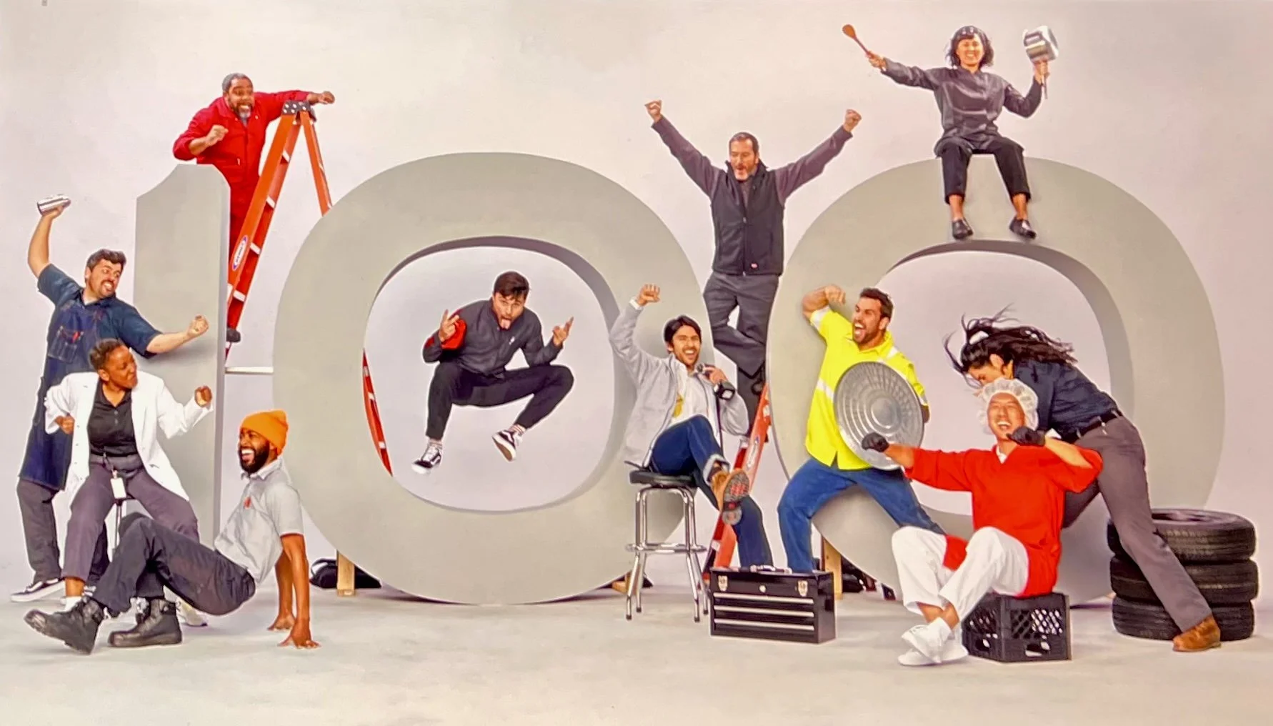 Group of diverse people posing around large gray letters spelling 'Dad', some sitting, jumping, or standing, with props and tools, engaging in playful and energetic activities.